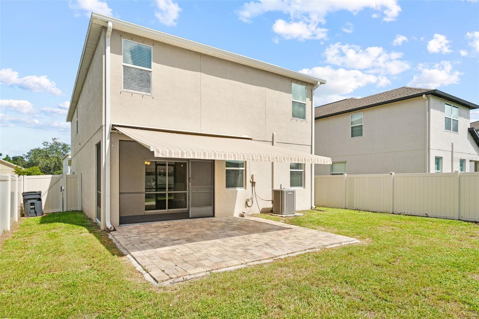 Rear Exterior & Patio – Rear view of the two-story home showcasing the screened lanai, extended paver patio, and fenced backyard. - 13728 REINDEER CIR, HUDSON