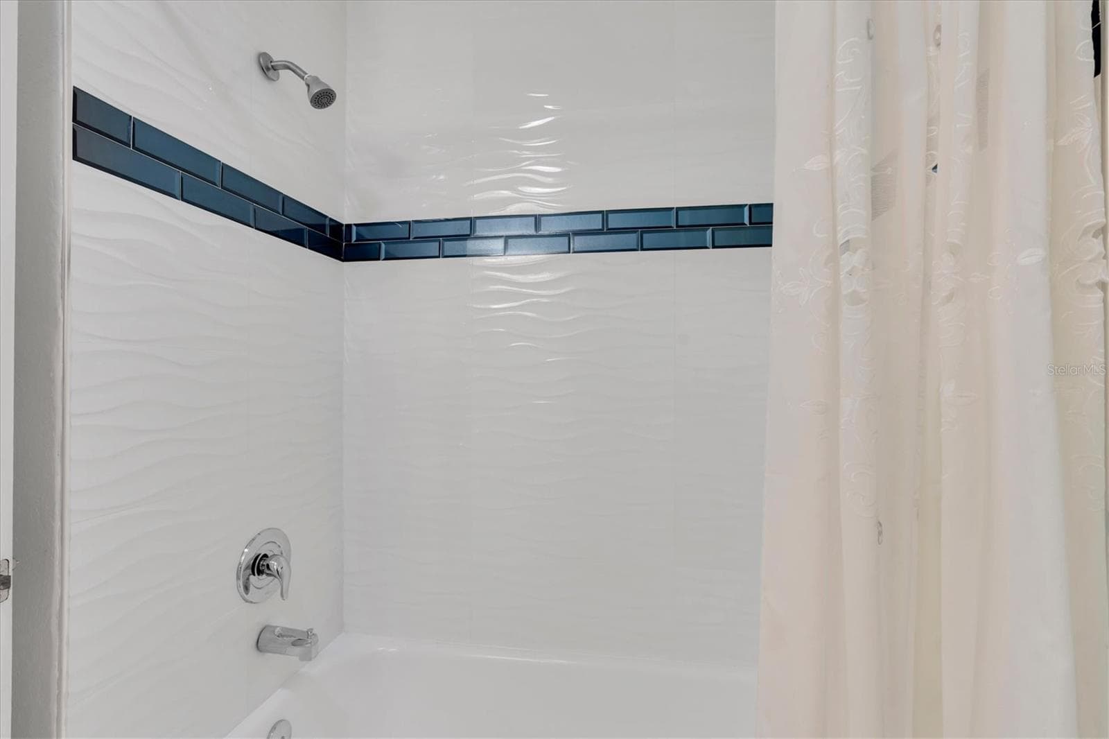 The shower area is surrounded by porcelain tile with attractive blue tile accents. - 6501 MOCKINGBIRD WAY S, GULFPORT