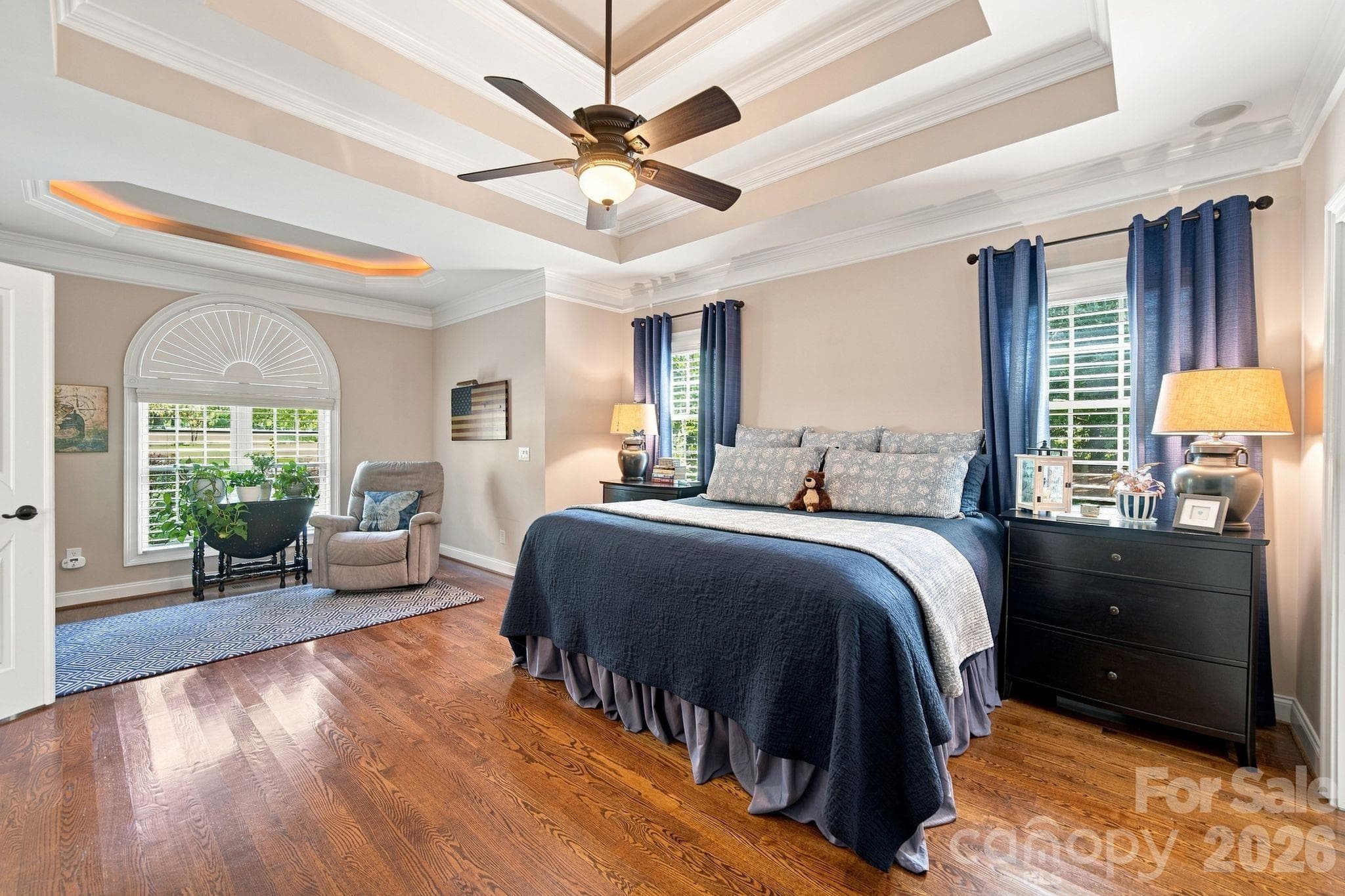 Experience luxury living in this main floor primary bedroom, featuring a cozy private sitting area, elegant multiple tray ceilings, immersive surround sound, and a stylish en suite for your ultimate comfort. - 1001 Heritage Acres Drive, Weddington