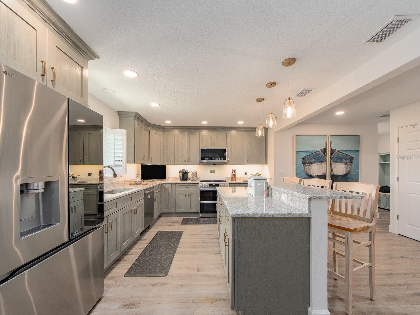 Tastefully remodeled kitchen centered around an expansive waterfall-edge island with bar seating, complimented by abundant cabinetry, high-end stainless-steel appliances, designer pendant lighting, and elevated finishes throughout. - 1207 TIMBERBROOKE DR, PALM HARBOR