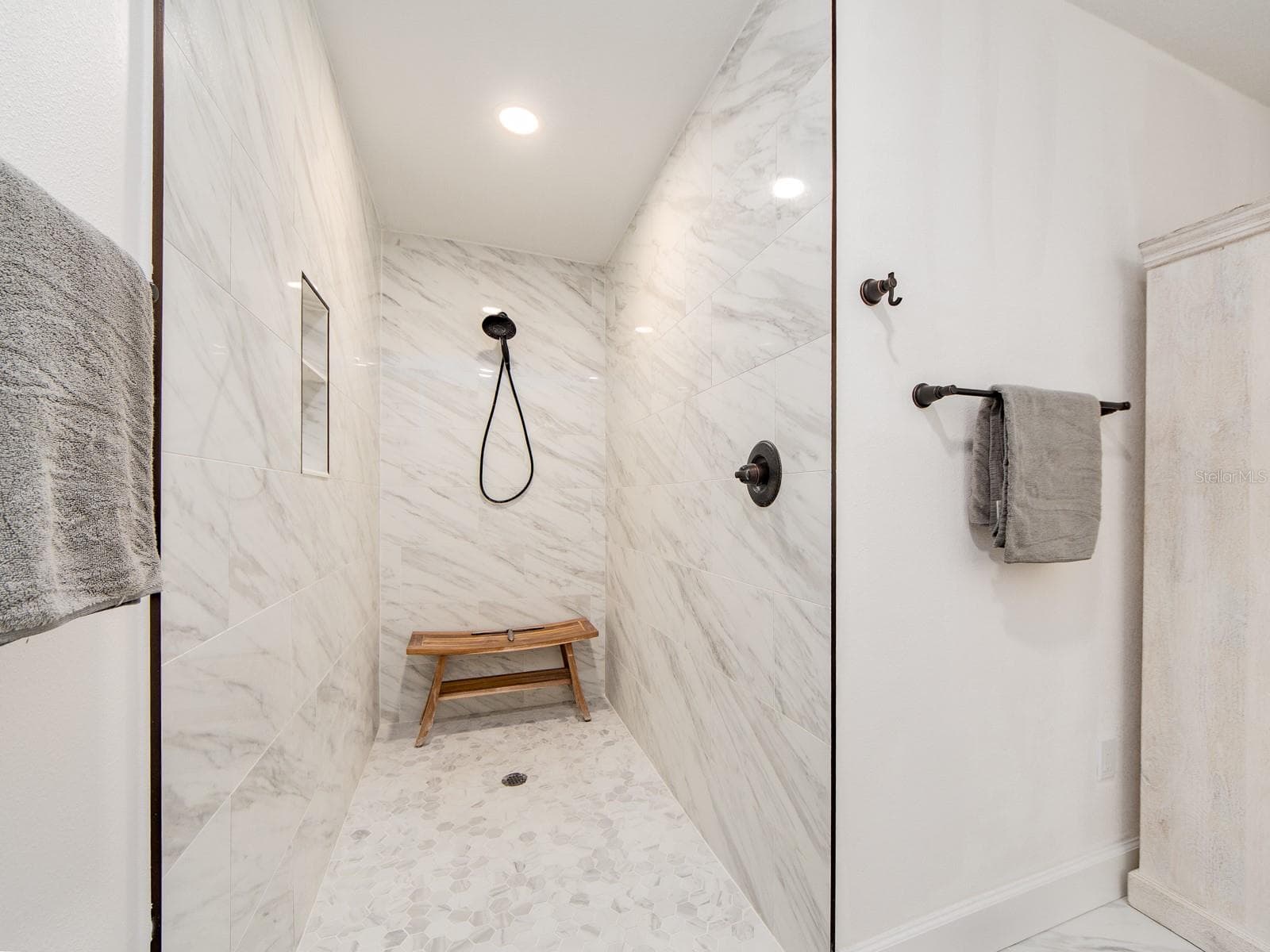 Start and end your day in this gorgeous spa-like setting! This oversized shower features a sleek doorless design, dramatic floor-to-ceiling marble-look tile, a convenient built-in niche and contrasting matte black fixtures for a striking modern finish. - 1207 TIMBERBROOKE DR, PALM HARBOR