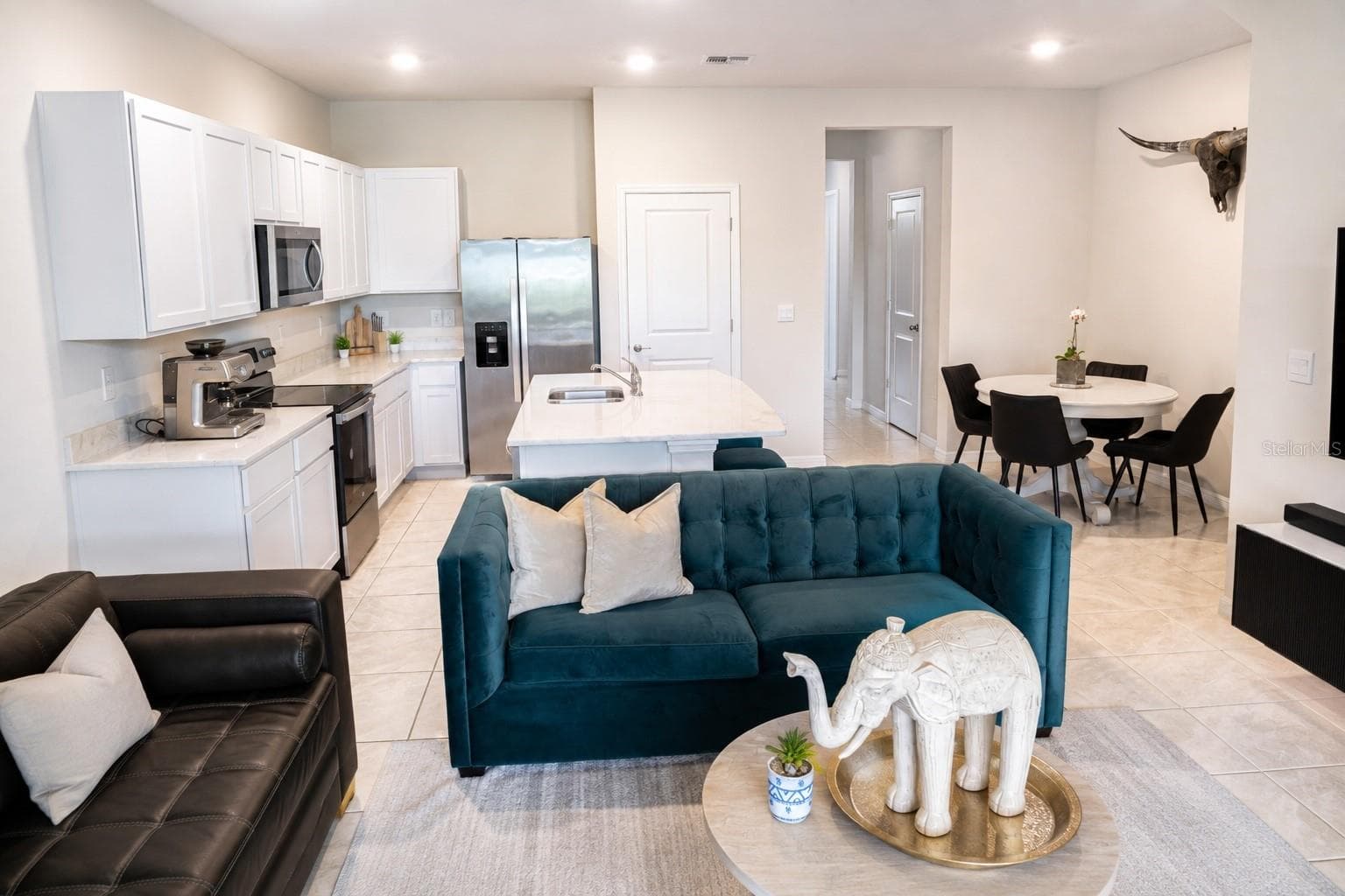 Open-concept kitchen with white cabinetry, quartz island, and stainless steel appliances flows seamlessly into the dining area — perfect for entertaining. - 17632 CRESCENT MOON LOOP, BRADENTON