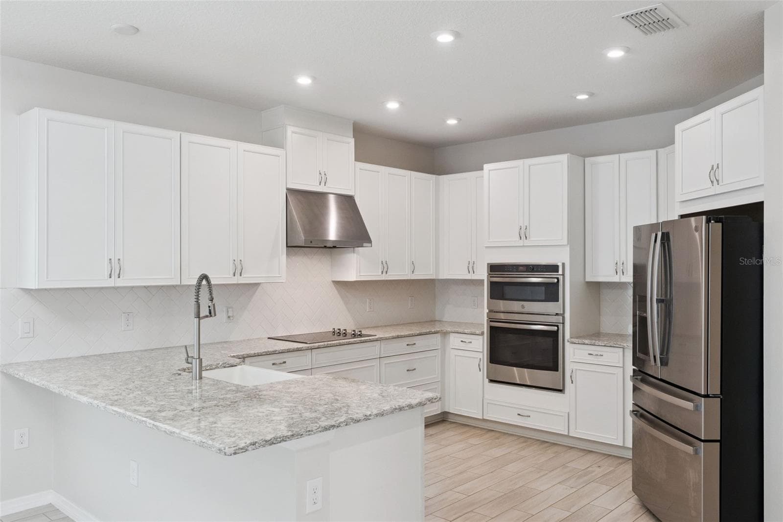 Kitchen – Bright kitchen features abundant white cabinetry, granite countertops, a tile backsplash, recessed lighting, stainless steel appliances, double wall ovens, and generous counter space for everyday prep. - 1287 VERDANT GLADE PL, WINTER PARK