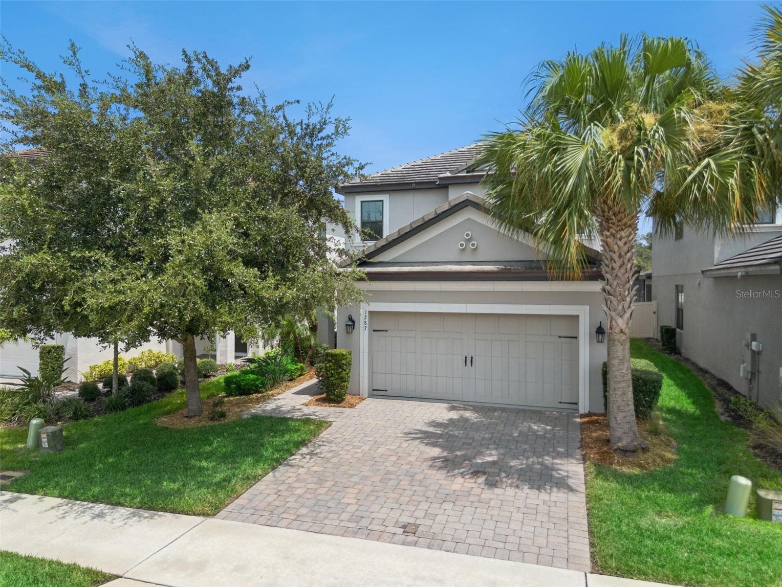 Wide exterior view highlights the two-story design, tile roof, established landscaping, palm trees, and attractive paver driveway. - 1287 VERDANT GLADE PL, WINTER PARK