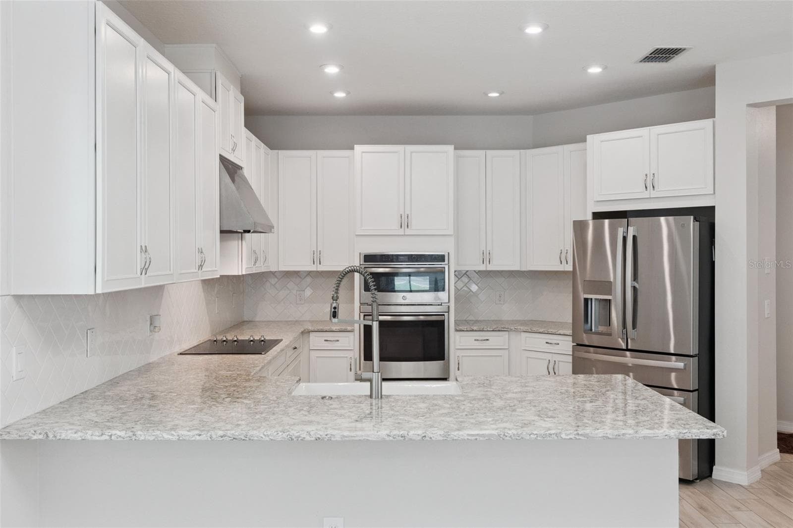 Kitchen – Spacious kitchen features abundant white cabinetry, granite countertops, a classic tile backsplash, stainless steel appliances, double wall ovens, and a generous peninsula with farmhouse-style sink and statement faucet. - 1287 VERDANT GLADE PL, WINTER PARK