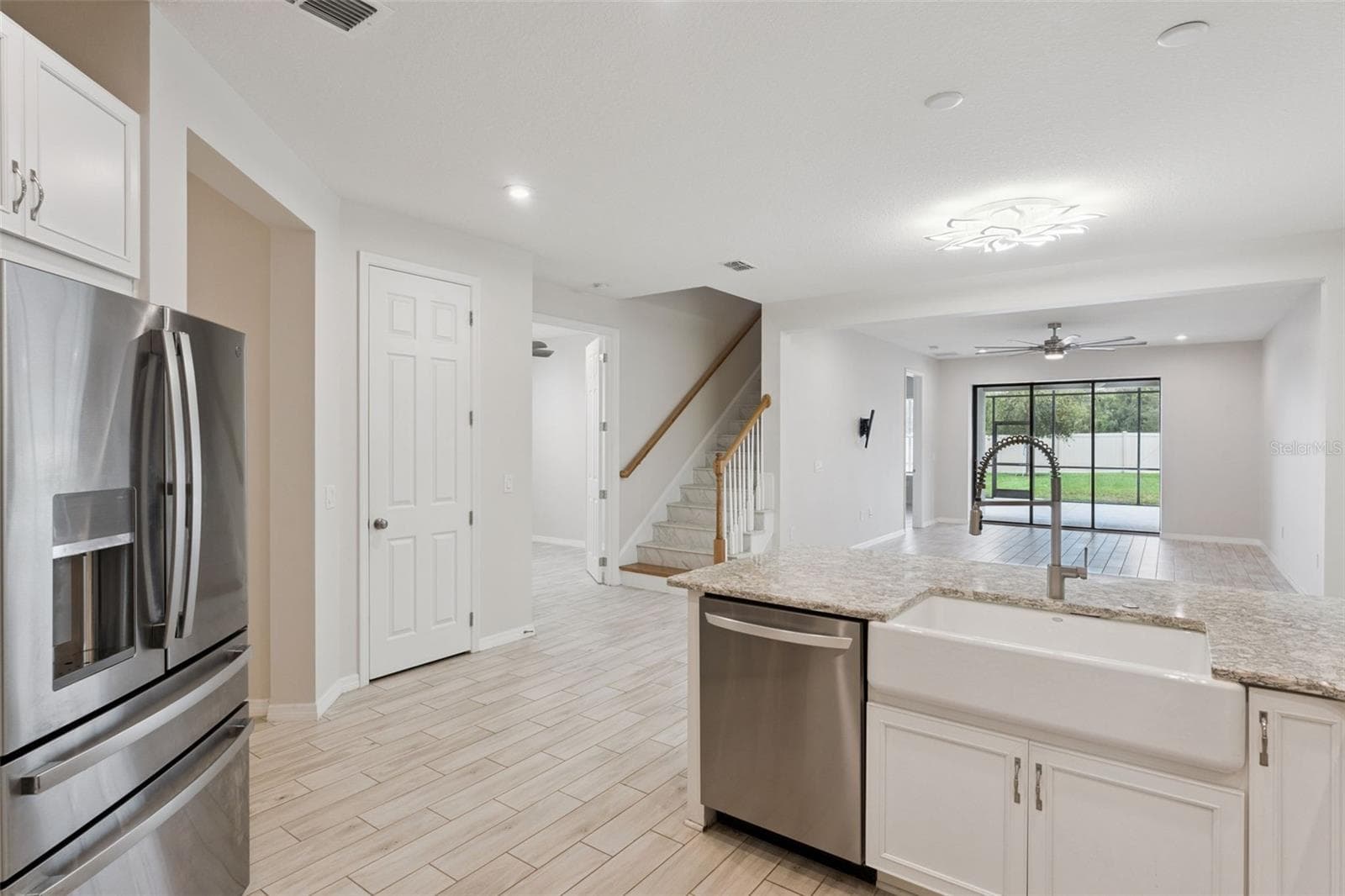Kitchen & Open Living Area – Open-concept kitchen connects seamlessly with the main living area and features granite countertops, a farmhouse-style sink, stainless steel appliances, and a large peninsula overlooking the room and screened patio beyond. - 1287 VERDANT GLADE PL, WINTER PARK
