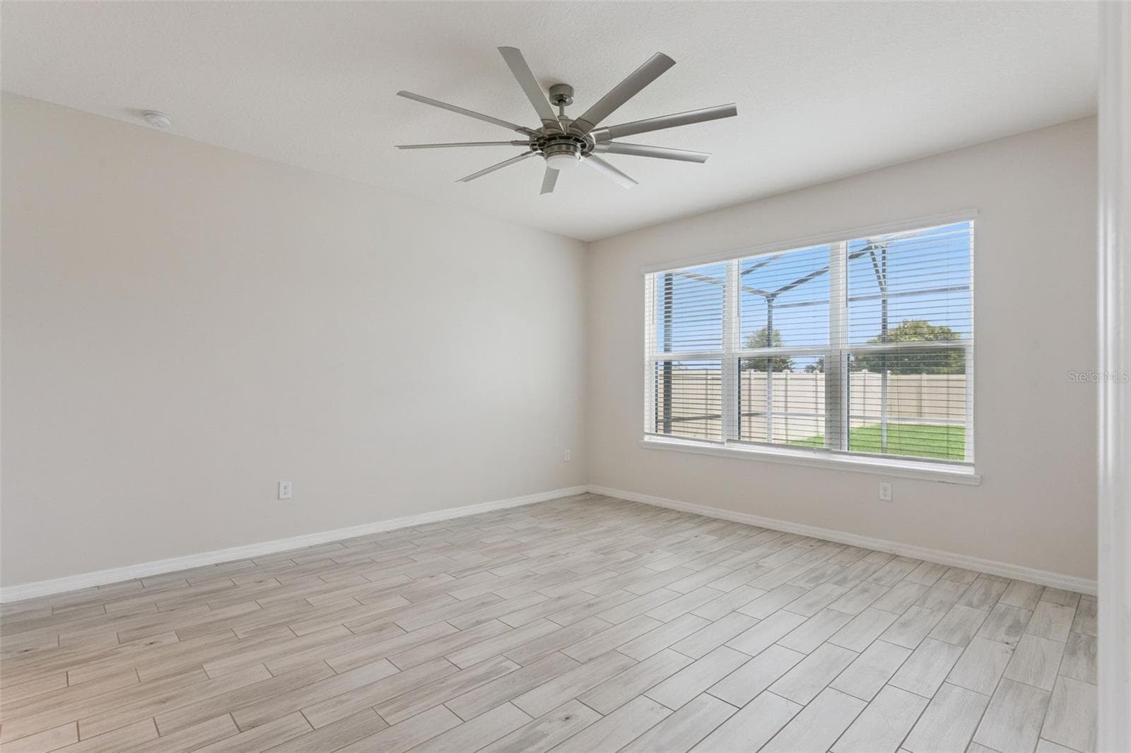 Primary Bedroom – Main-level primary bedroom offers generous proportions, wood-look tile flooring, a statement ceiling fan, and a wide window bringing in abundant natural light. - 1287 VERDANT GLADE PL, WINTER PARK