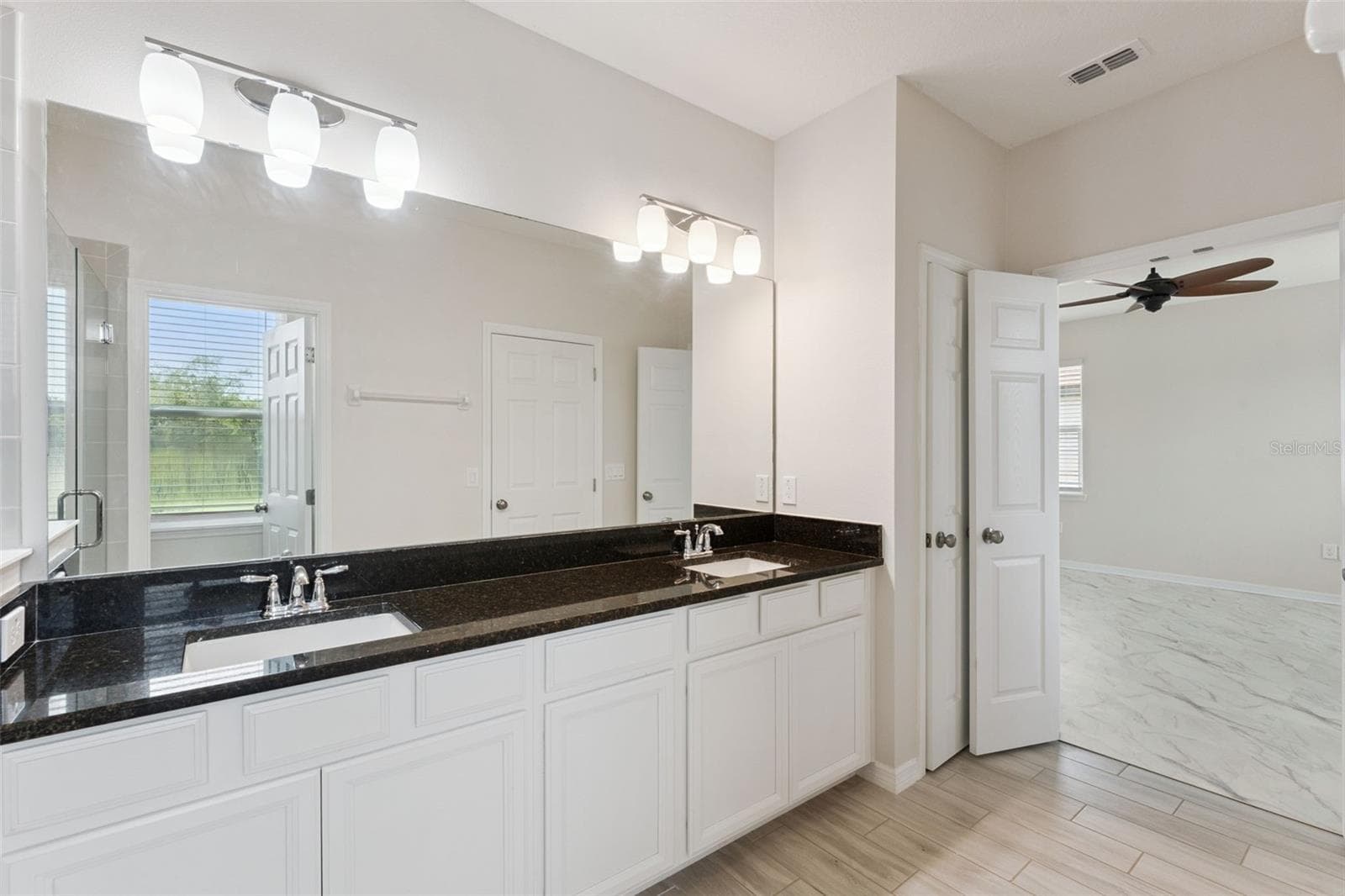 2nd Primary Bathroom – Spacious primary bath features an extended dual-sink vanity with dark stone countertop, abundant cabinetry, a large wall mirror, and bright vanity lighting. - 1287 VERDANT GLADE PL, WINTER PARK