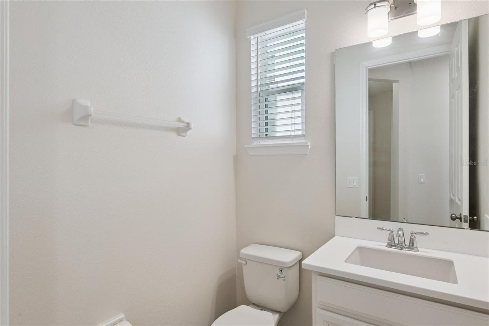 Downstairs Common Area Bathroom – Convenient main-level half bath features a crisp white vanity, large mirror, contemporary lighting, and a window that brings natural light into the space. - 1287 VERDANT GLADE PL, WINTER PARK