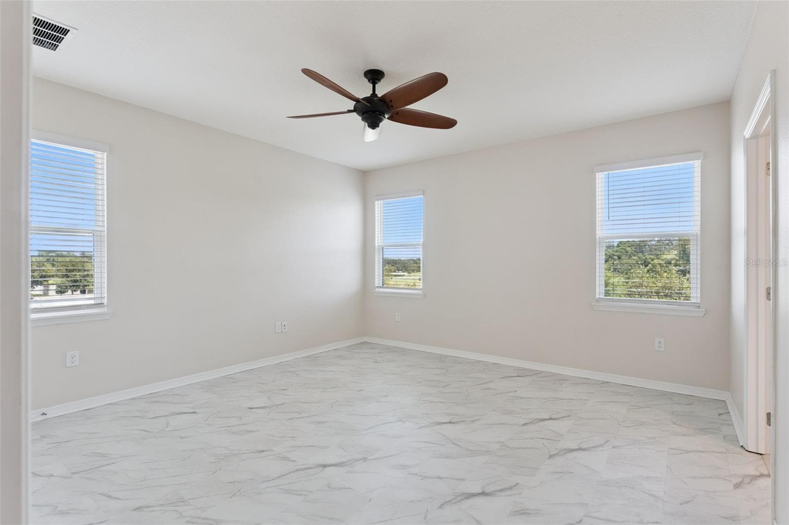 2nd Primary Suite (Upstairs)  – Spacious upstairs primary bedroom with marble-look tile flooring, a ceiling fan, and multiple windows providing abundant natural light. - 1287 VERDANT GLADE PL, WINTER PARK
