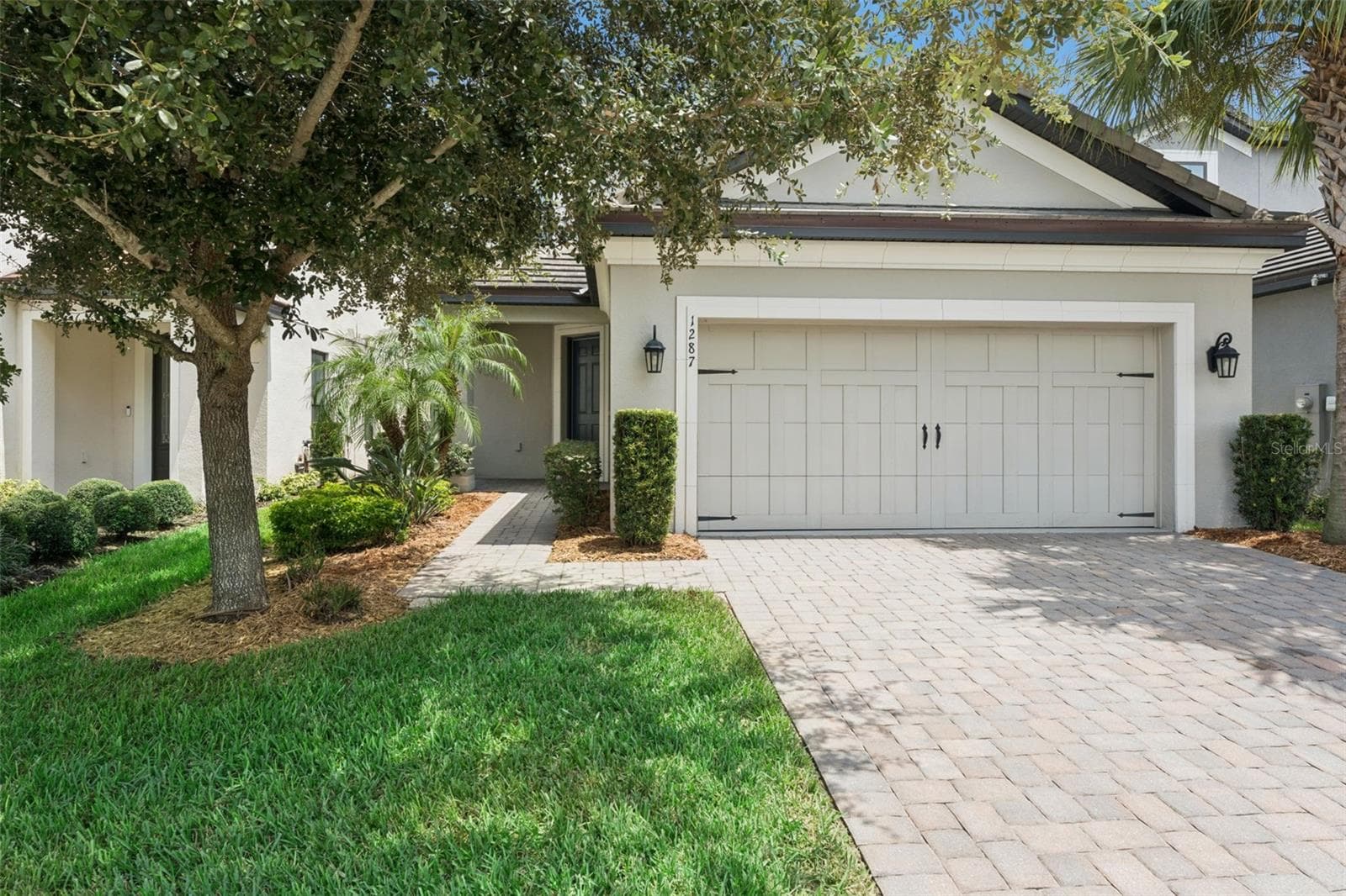Front Exterior – Welcoming front exterior with mature landscaping, a paver driveway, and a two-car garage with carriage-style detailing. - 1287 VERDANT GLADE PL, WINTER PARK