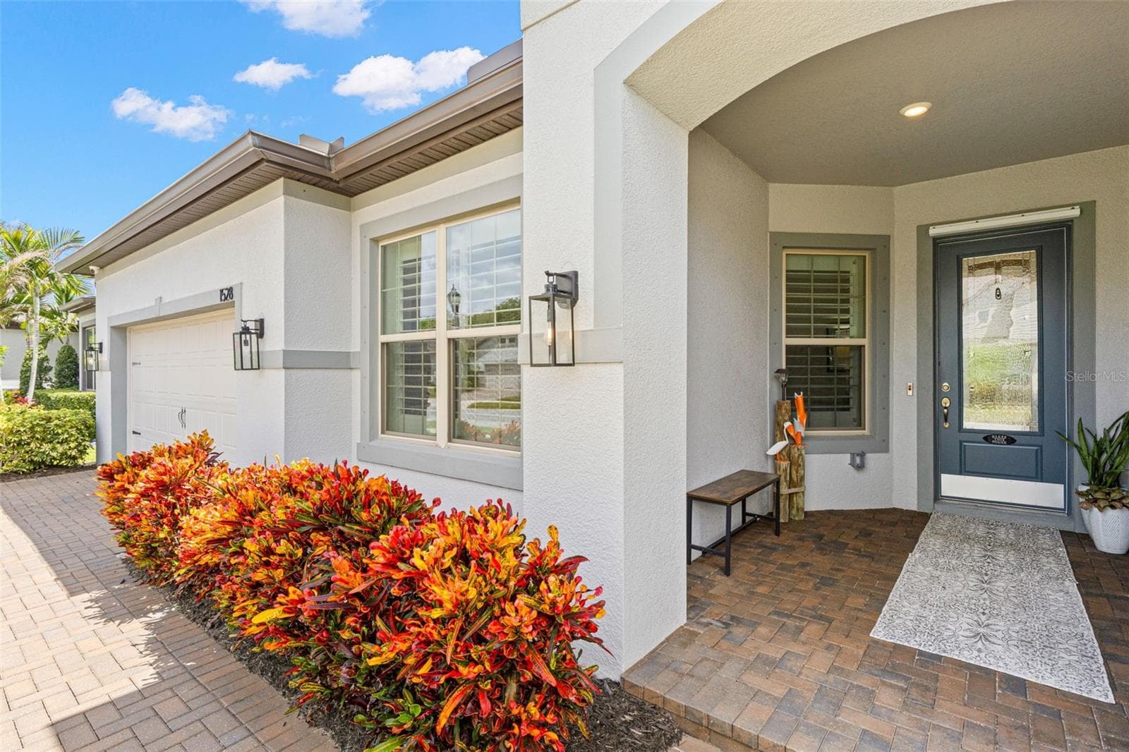 The brick-paver walkway continues to a deep covered entry, framed by modern lantern-style lighting and a stately arched opening that gives the home a welcoming sense of arrival. - 1528 FOREST GLEN CT, PALM HARBOR