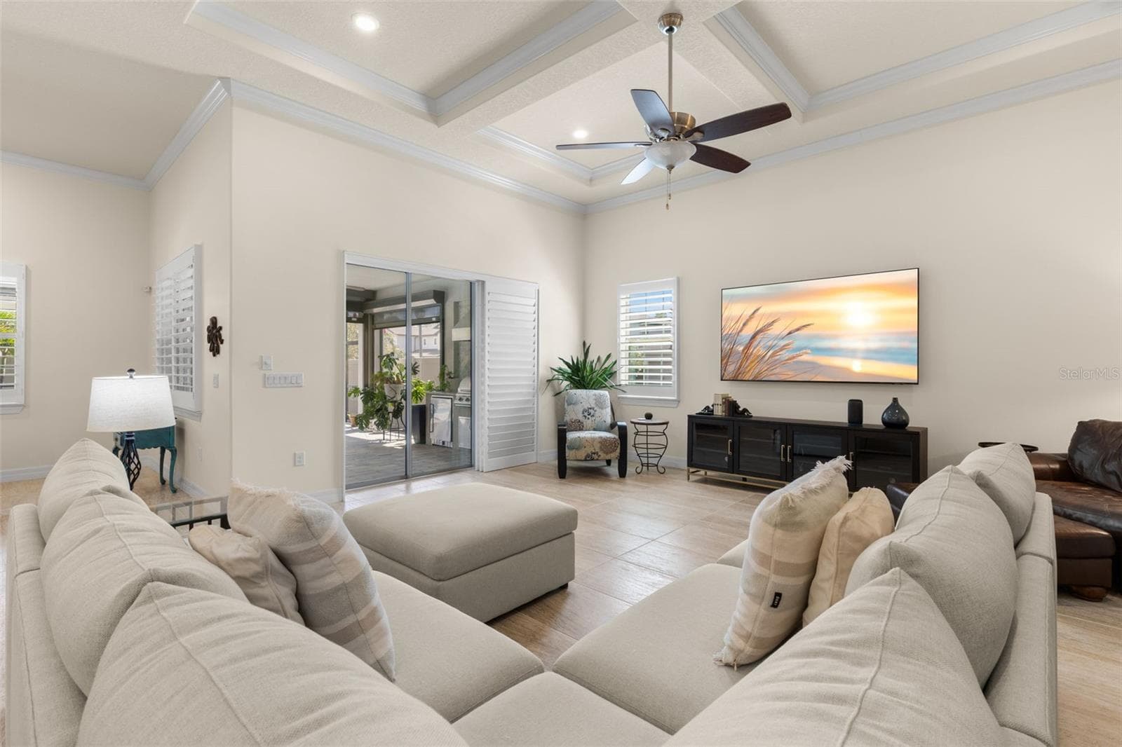 A soft, neutral color palette keeps the great room feeling light and inviting, while the dramatic tray ceiling, ceiling fan and plantation shutters add polished detail. Wide sliding glass doors create an easy connection to the screened lanai and pool. - 1528 FOREST GLEN CT, PALM HARBOR