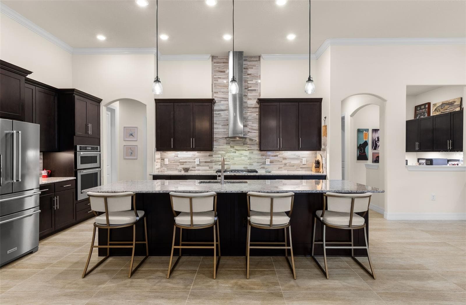 The kitchen is built to be used and enjoyed, with a generous granite-topped island offering seating for four, rich cabinetry, double ovens and a gas cooktop beneath a striking stainless hood and full-height tile backsplash. Pendant and recessed lighting keep the space bright, while the open design makes it easy to stay connected to the living and dining areas. - 1528 FOREST GLEN CT, PALM HARBOR