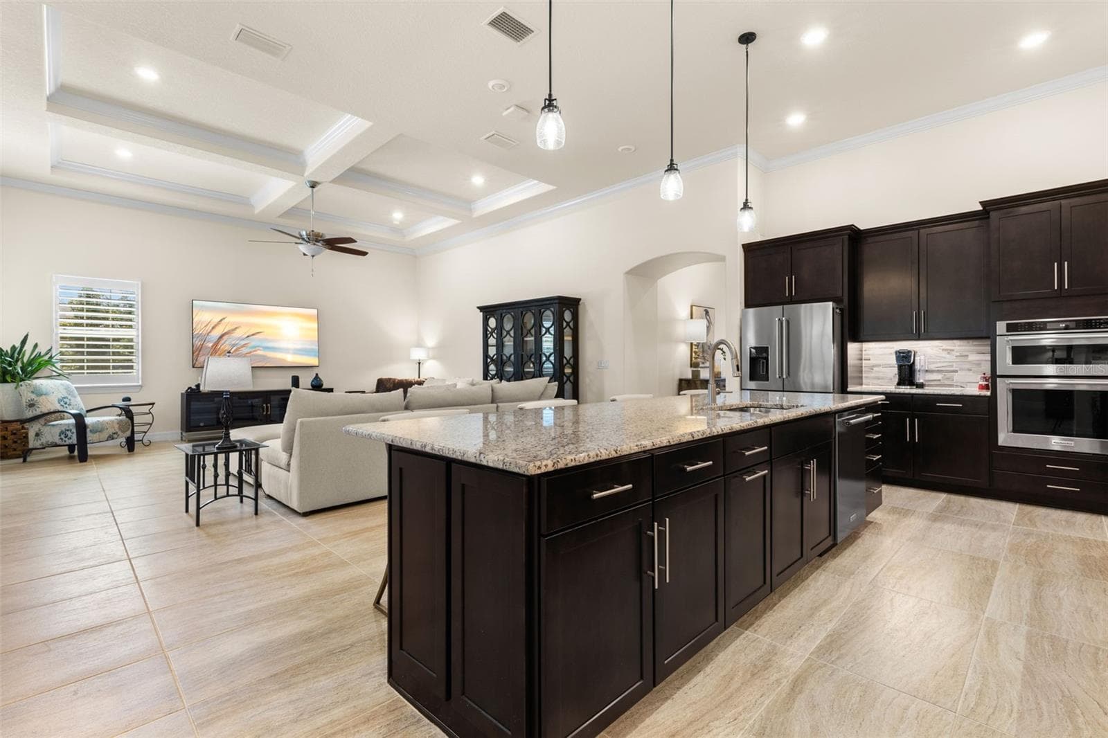 At the heart of the home, the kitchen’s oversized island brings everyone together, with generous workspace, abundant storage, and an easy connection to the great room beyond. Rich cabinetry and granite counters add warmth and contrast, while the soaring ceiling details carry seamlessly through the open living space. - 1528 FOREST GLEN CT, PALM HARBOR