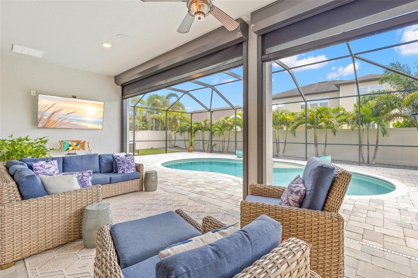 This is Florida living done right: a spacious covered lounge area overlooks the pool, with a ceiling fan and wall-mounted TV creating an easy spot to relax in the shade. A Kevlar hurricane protection system adds an important layer of protection to the lanai when needed. - 1528 FOREST GLEN CT, PALM HARBOR