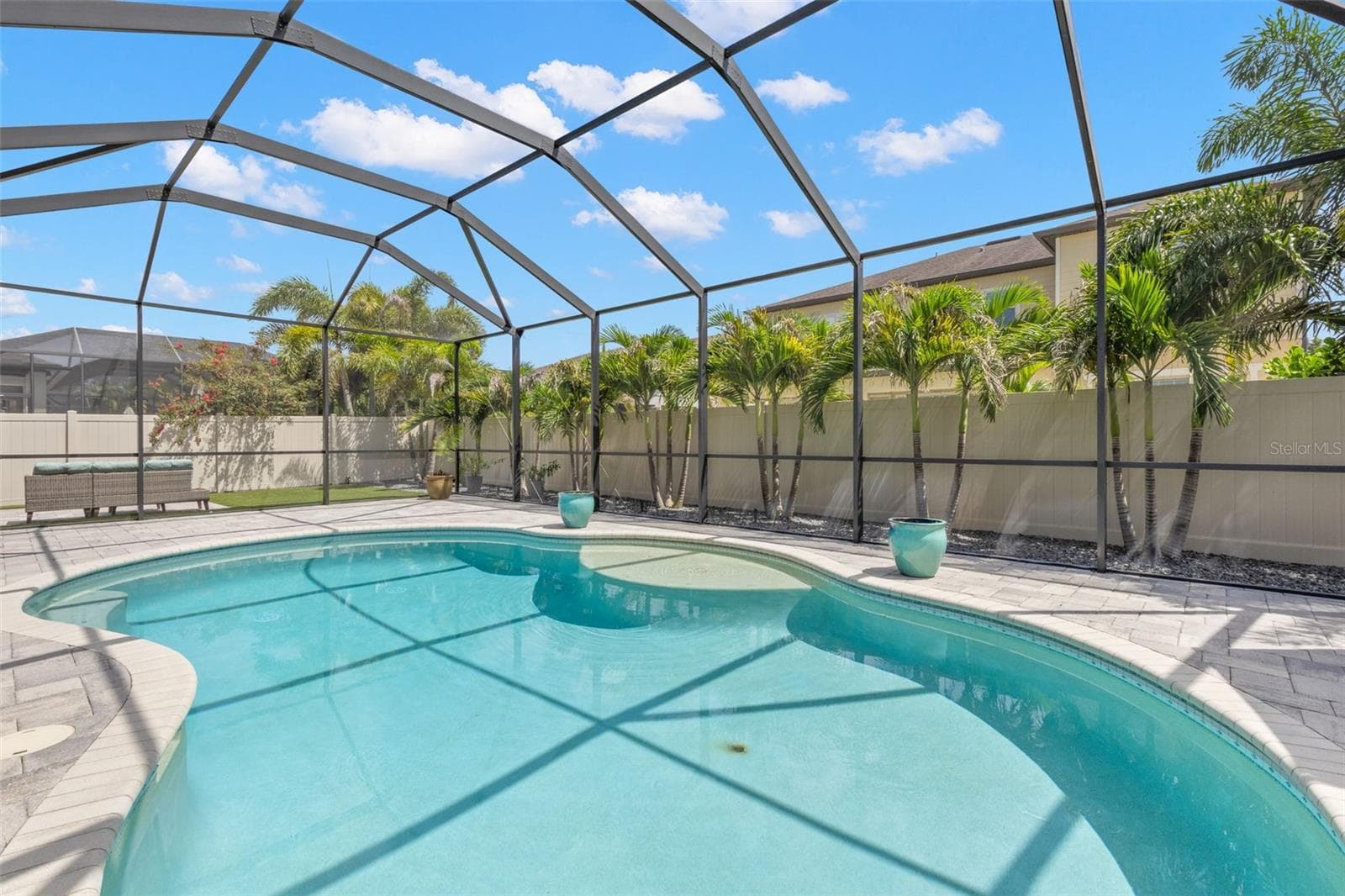 A row of lighted palms creates a lush tropical backdrop around the screened pool, adding privacy by day and taking on a whole new look after dark with landscape lighting. The sun shelf offers an easy place to cool off without leaving the water. - 1528 FOREST GLEN CT, PALM HARBOR