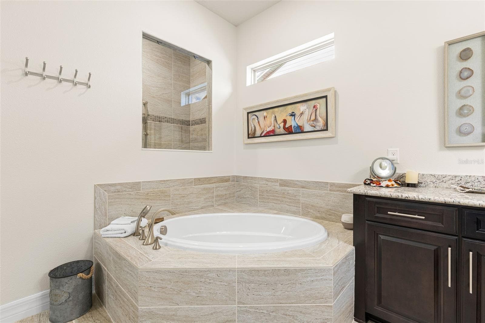 The garden tub creates a relaxing focal point in the primary bath, wrapped in oversized tile with a high transom window bringing in natural light. A pass-through opening offers a glimpse of the separate tiled shower just beyond. - 1528 FOREST GLEN CT, PALM HARBOR