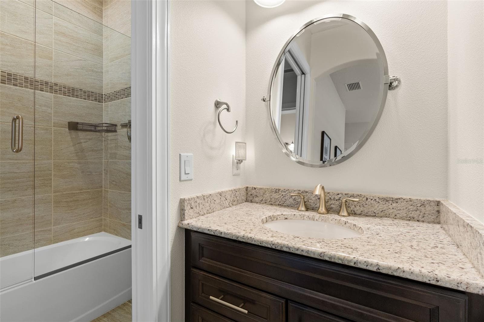 One of two separate vanity areas serving the Jack-and-Jill bath features a granite counter and rich cabinetry, while the shared bathing area includes a glass-enclosed tub and shower. Each adjoining bedroom has its own sink and vanity space, a smart detail that adds everyday function. - 1528 FOREST GLEN CT, PALM HARBOR