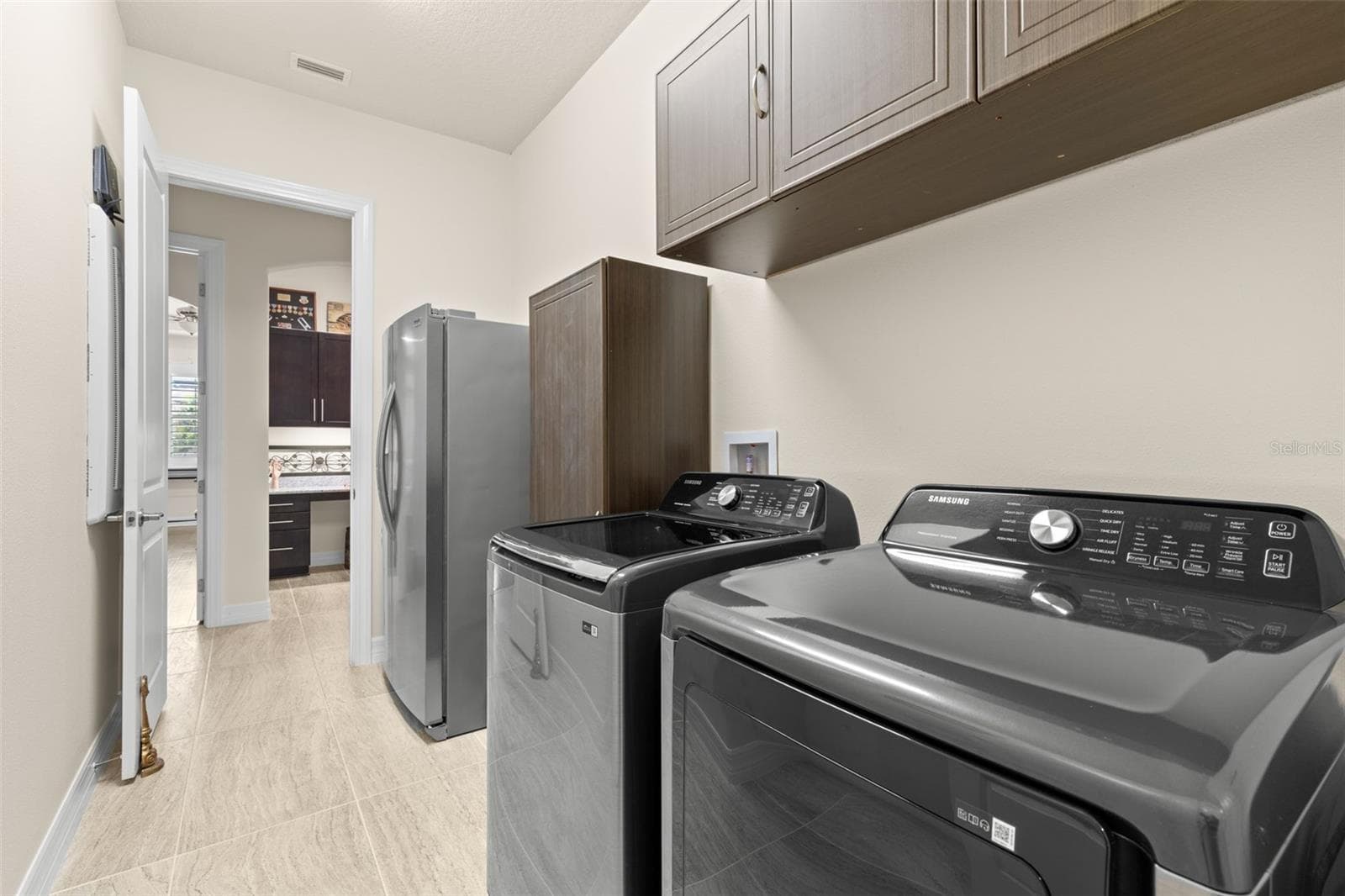 The spacious laundry room keeps everyday chores organized with a full-size washer and dryer, abundant upper cabinetry and additional storage, all conveniently positioned between the kitchen and garage-entry area. The refrigerator shown in the laundry room does not convey. - 1528 FOREST GLEN CT, PALM HARBOR