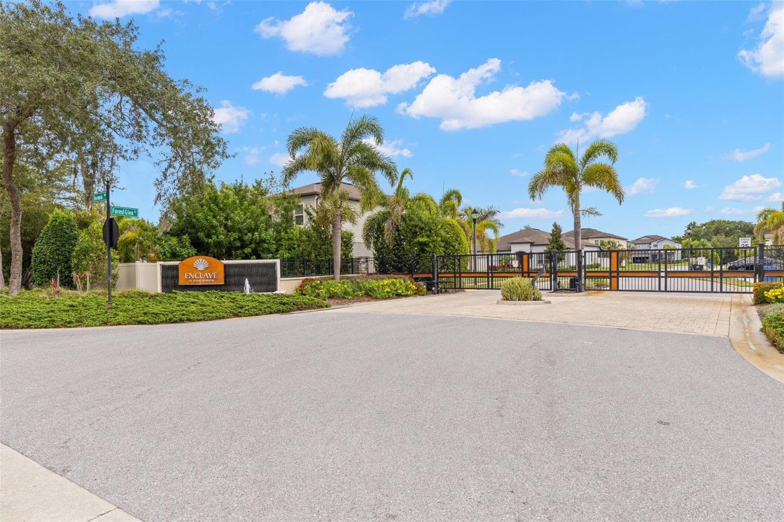 The gated entrance to Enclave at Palm Harbor sets the tone with tropical landscaping, palms and a polished streetscape, creating a welcoming sense of arrival before you ever reach the home. - 1528 FOREST GLEN CT, PALM HARBOR