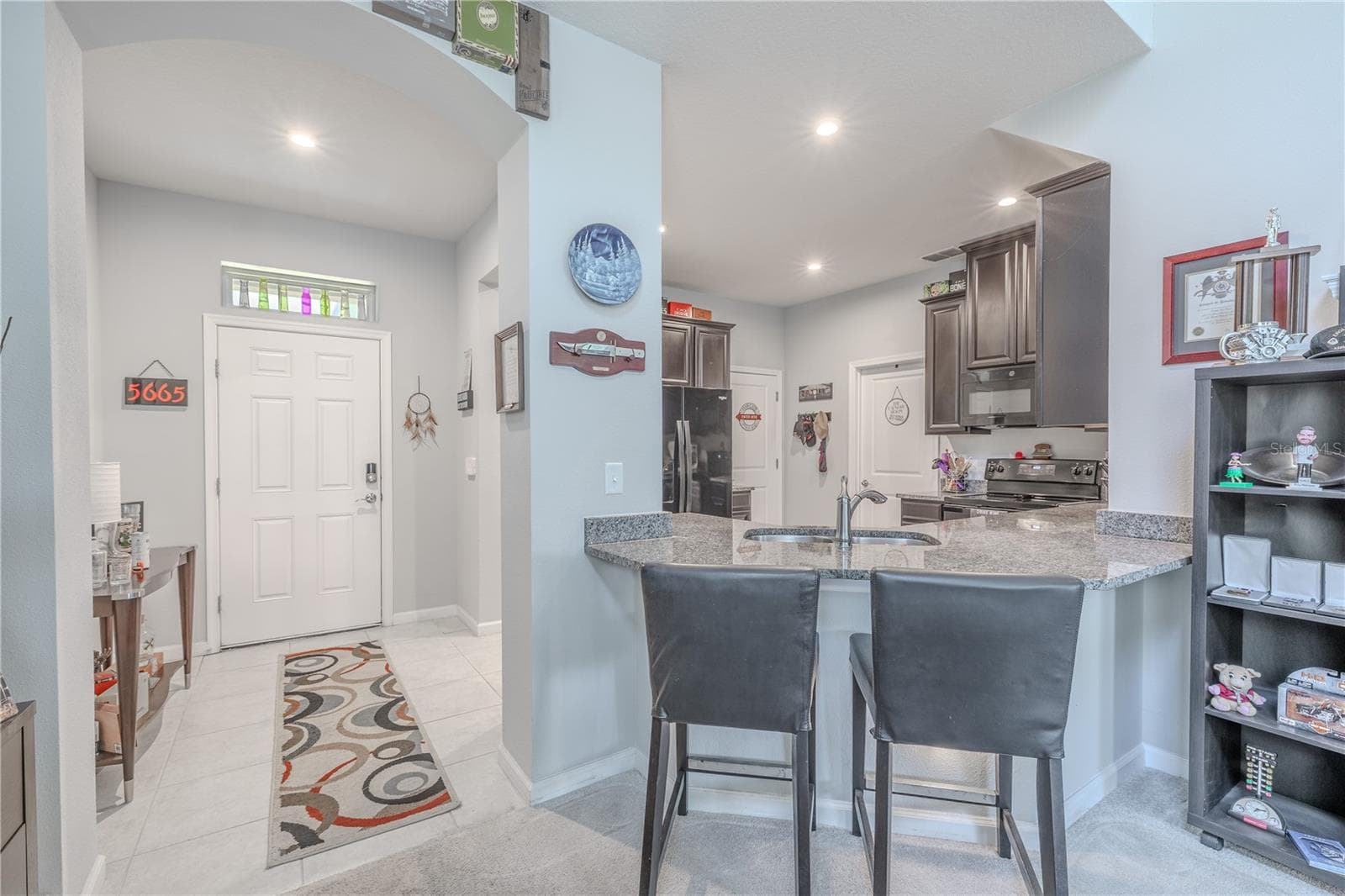 The tiled entry opens directly to the kitchen, where a granite-topped peninsula with bar seating creates a casual gathering spot while maintaining an open connection to the main living area. - 3029 JACOB CROSSING LN, HOLIDAY