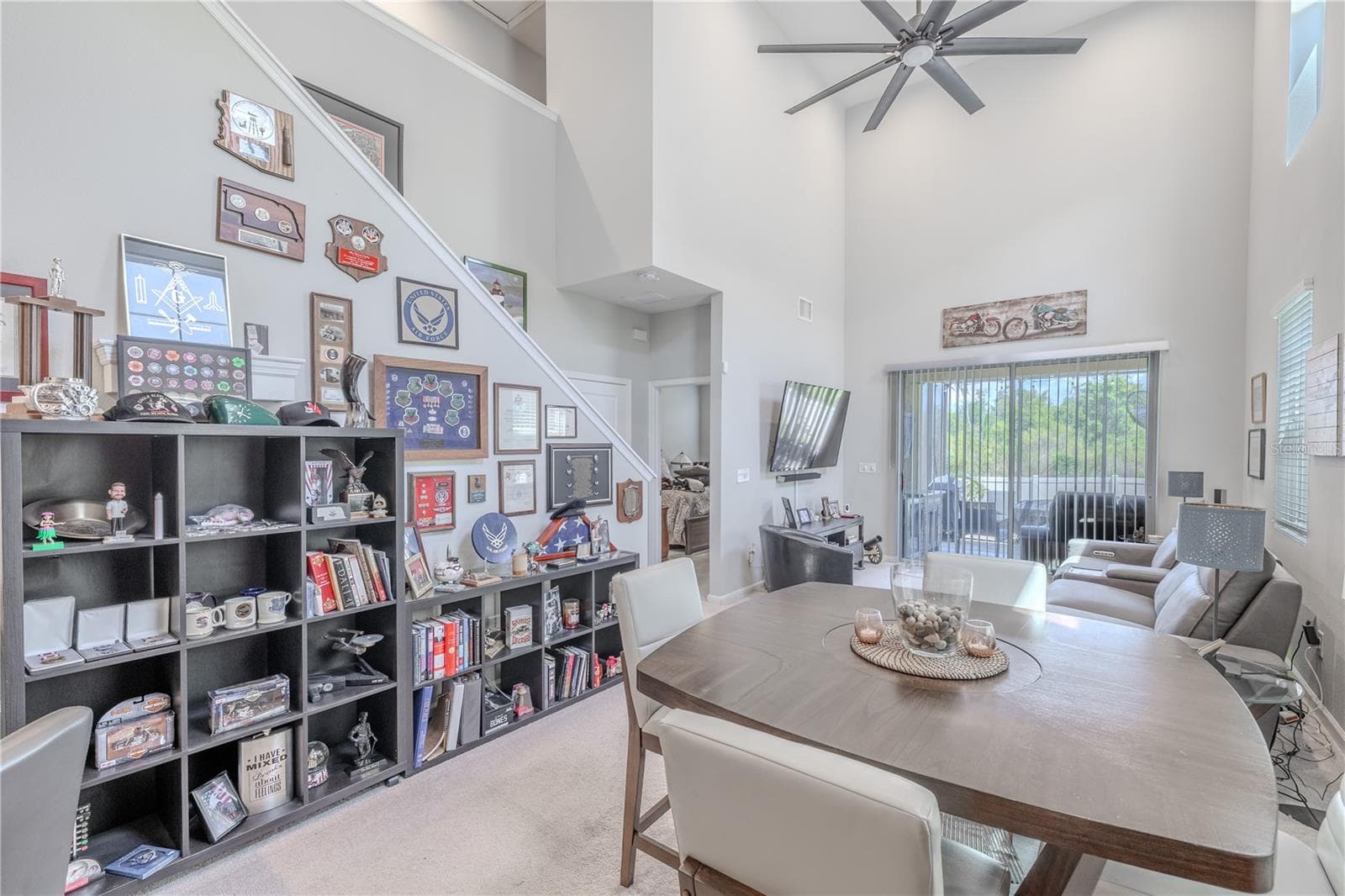 The staircase rises alongside the open living and dining area, where the dramatic ceiling height and rear sliders create a strong sense of space and connection to the screened lanai. - 3029 JACOB CROSSING LN, HOLIDAY
