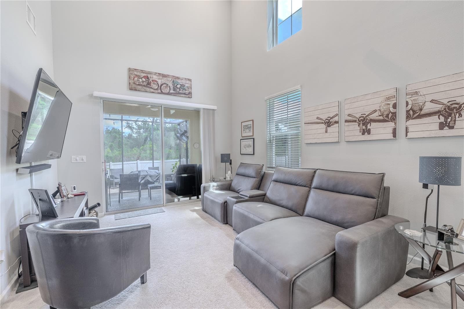 The living room offers plenty of space for comfortable seating beneath the soaring ceiling, with a tall window and sliding glass doors bringing in natural light and opening to the screened lanai. - 3029 JACOB CROSSING LN, HOLIDAY