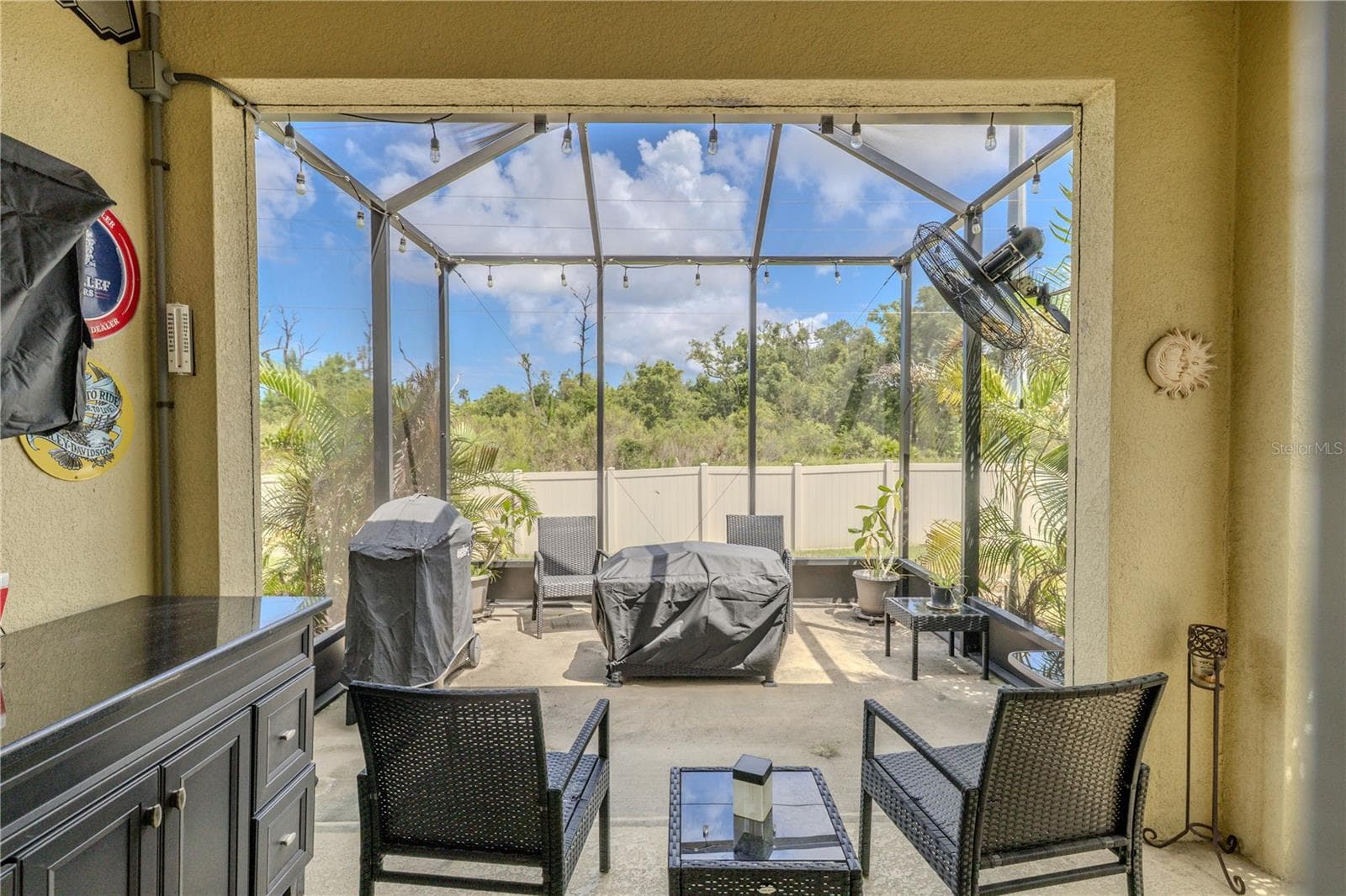 The covered lanai flows into an extended screened patio, creating two distinct outdoor living areas with string lights overhead and a leafy green-space backdrop beyond the privacy fence. - 3029 JACOB CROSSING LN, HOLIDAY