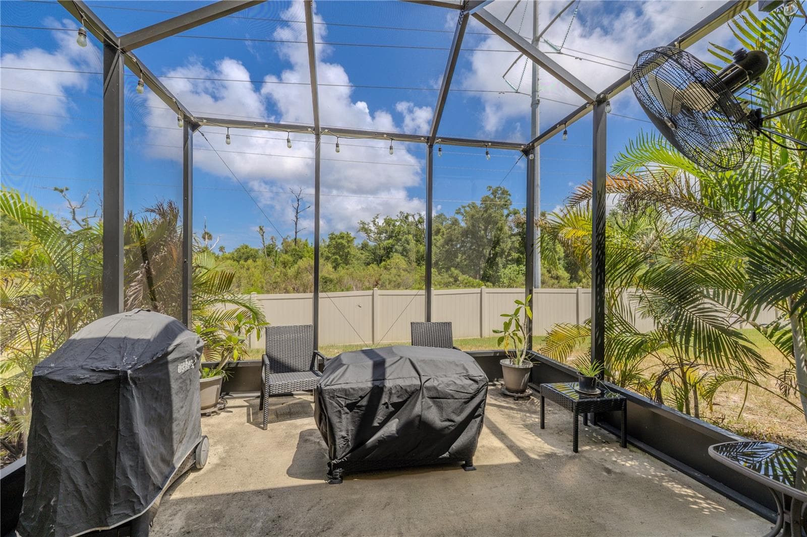 The extended screened patio creates a sunny outdoor retreat with room for grilling and seating, framed by tropical plantings and a privacy fence with expansive greenery beyond. - 3029 JACOB CROSSING LN, HOLIDAY