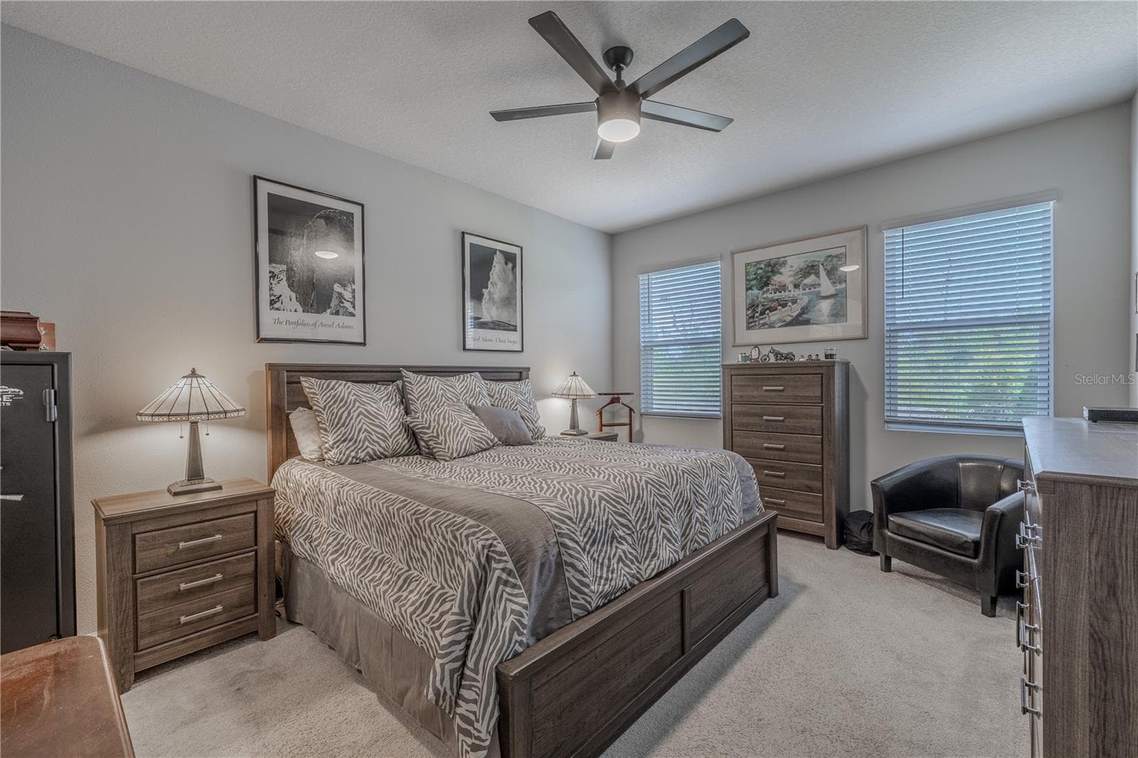 Generously proportioned, the first-floor primary bedroom easily accommodates a full furniture suite plus a sitting area, with a ceiling fan, two large windows, neutral walls and coordinating carpet creating a calm, comfortable setting. - 3029 JACOB CROSSING LN, HOLIDAY