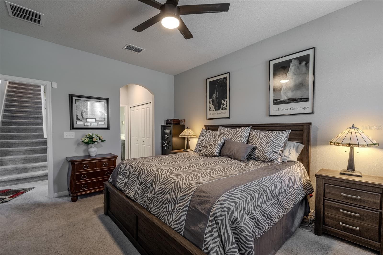 The spacious first-floor primary suite pairs a calm neutral palette with a ceiling fan and comfortable proportions, while an arched opening adds architectural character and leads toward the ensuite bath and walk-in closet. - 3029 JACOB CROSSING LN, HOLIDAY