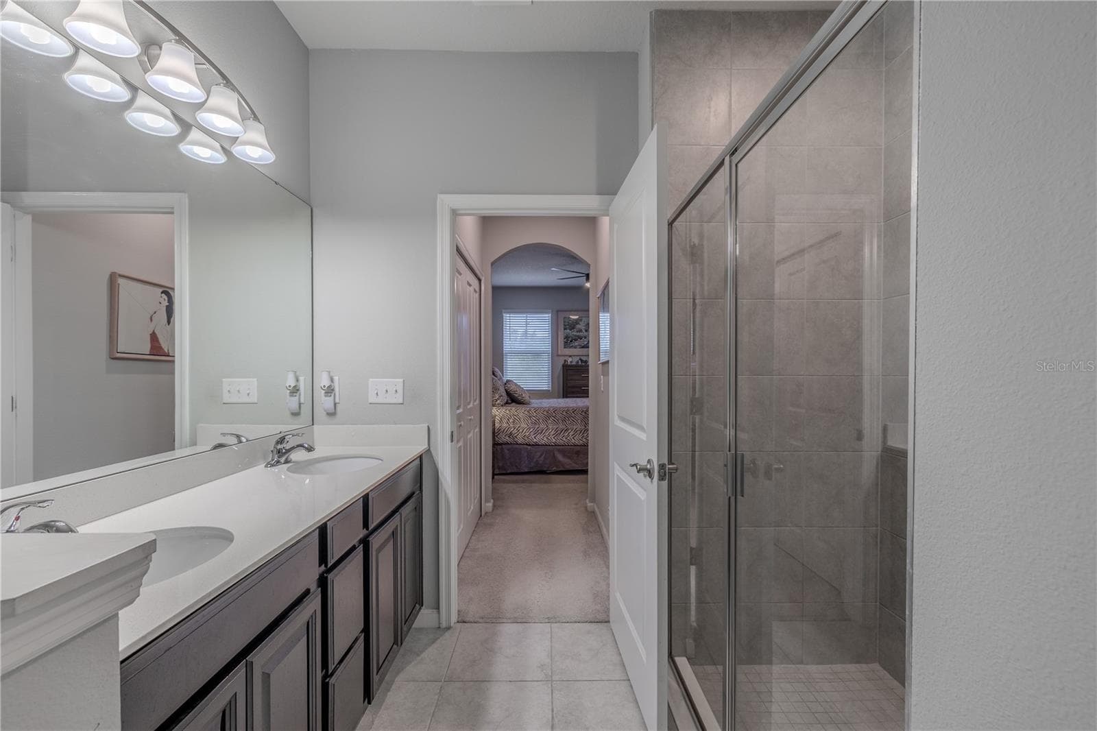 The primary bath pairs a long dual-sink vanity with a glass-enclosed tiled shower, while the direct sightline back to the bedroom reinforces the suite’s comfortable, connected layout. - 3029 JACOB CROSSING LN, HOLIDAY