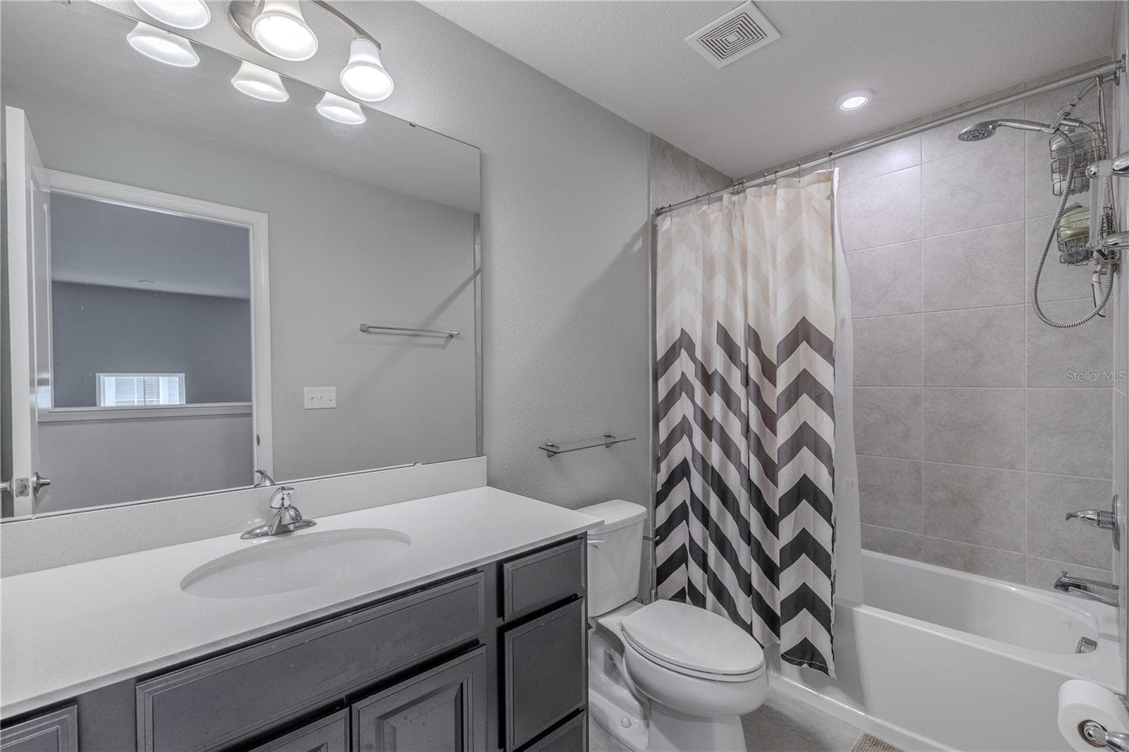 The second full bath combines a spacious single-sink vanity, oversized mirror and neutral finishes with a tiled tub-and-shower combination, creating a bright, functional space for family or guests. - 3029 JACOB CROSSING LN, HOLIDAY