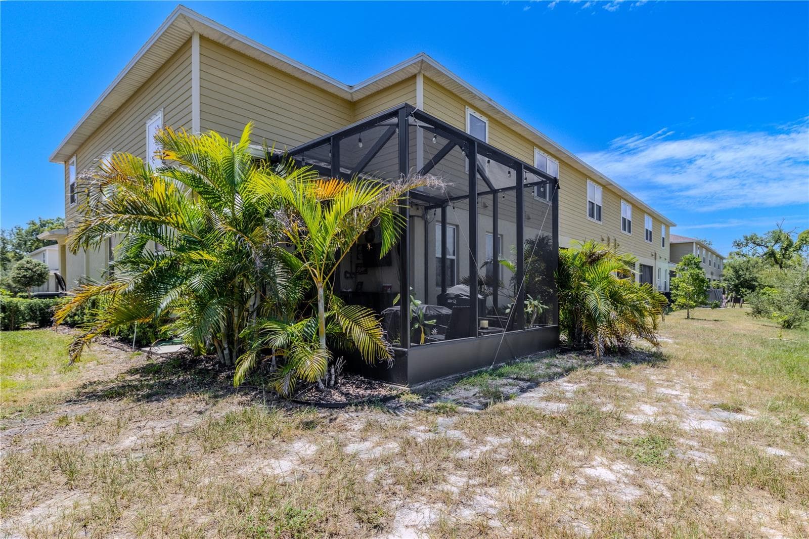 The rear exterior showcases the expanded screened lanai, wrapped in tropical landscaping and positioned along the end of the building for a more open outdoor setting. - 3029 JACOB CROSSING LN, HOLIDAY