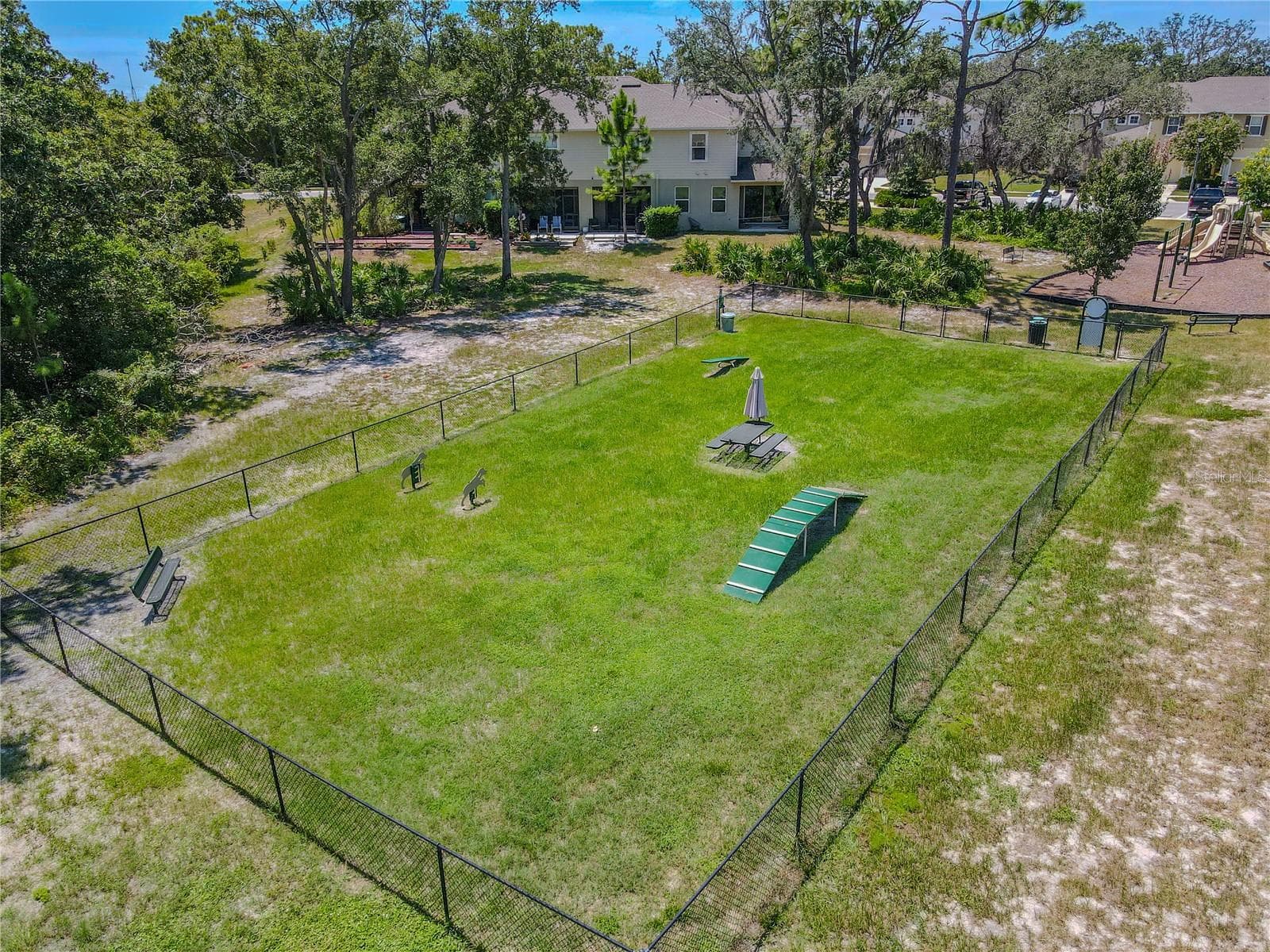 The community dog run offers a large fenced grassy area with agility equipment and bench seating, giving four-legged residents plenty of room to play. - 3029 JACOB CROSSING LN, HOLIDAY