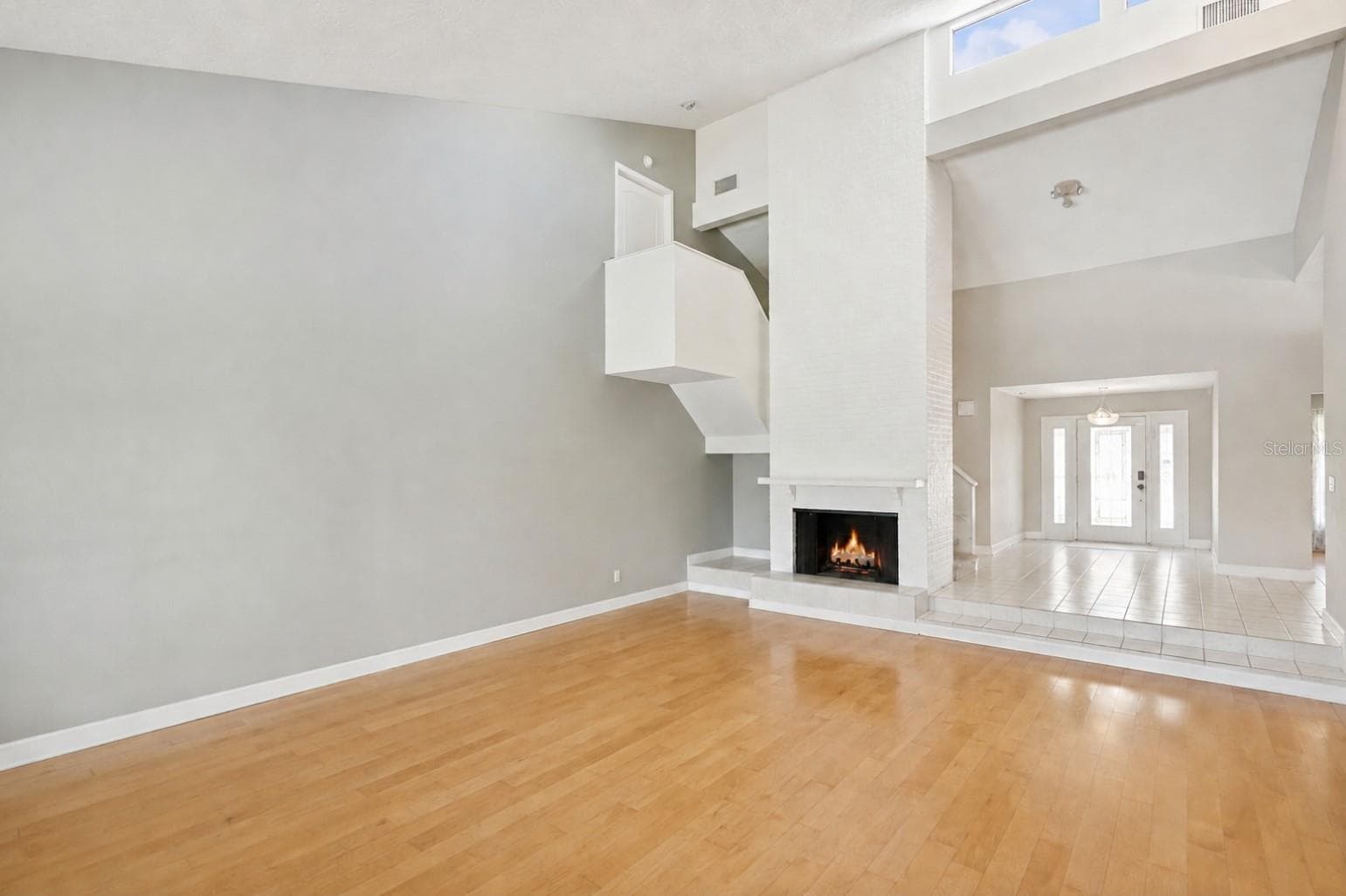 Inviting foyer and family room featuring a floor-to-ceiling brick fireplace, skylights that fill the space with natural light, and a staircase leading to three spacious upstairs bedrooms. - 25 LAKEWOOD CSWY, WINTER HAVEN