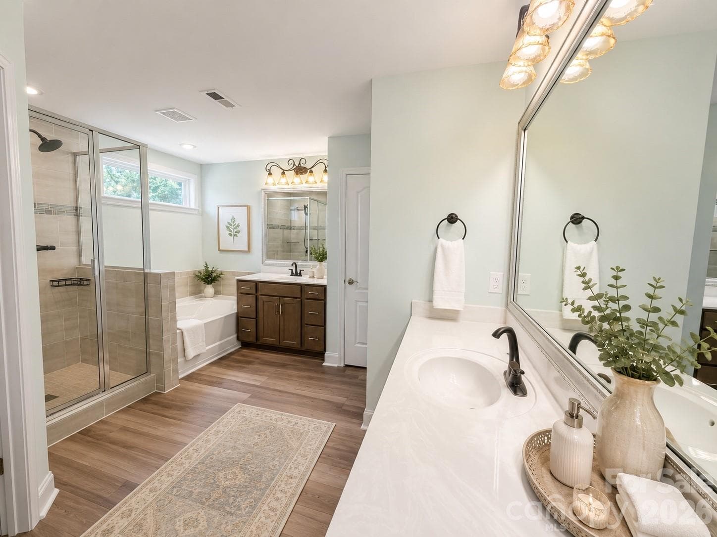 Primary Bathroom features dual vanities, upgraded faucets and lighting, upgraded flooring, standing shower features tile.  Transom window above tub for natural llighting and privacy.  Walk in Closet, linen closet and water closet included but not pictured. (photo has been virtually staged) - 1318 Poppy Way, Matthews