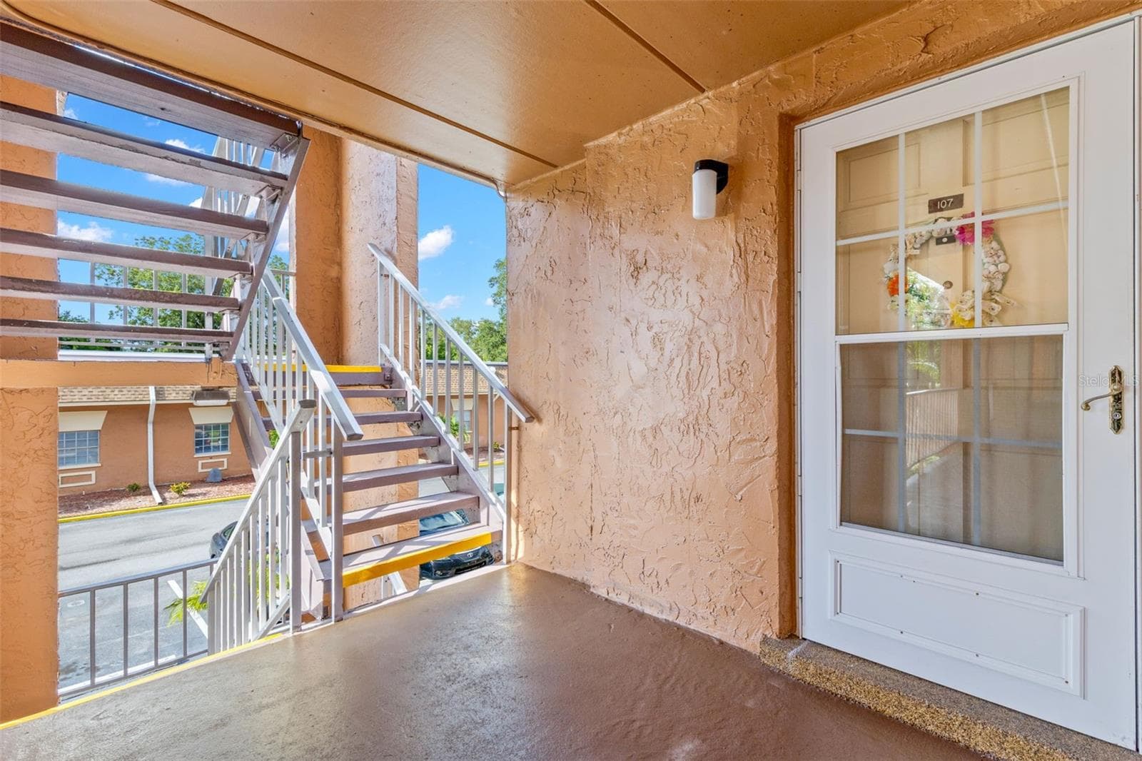 The covered exterior landing leads to a sheltered front entry, where a storm door adds another layer of light and ventilation before stepping inside. - 12760 INDIAN ROCKS RD #107, LARGO