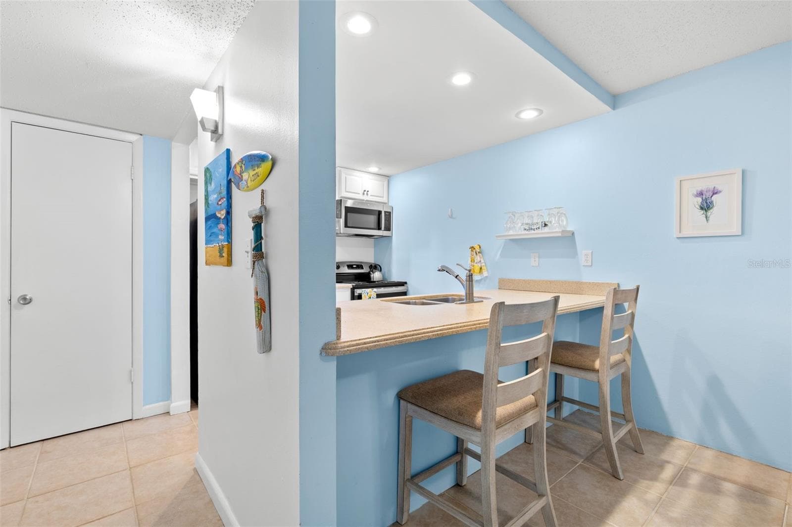 A closer look from the dining area shows the breakfast bar with seating for two, while the kitchen’s recessed lighting, Corian counters and open pass-through keep the space bright and connected to the rest of the condo. - 12760 INDIAN ROCKS RD #107, LARGO
