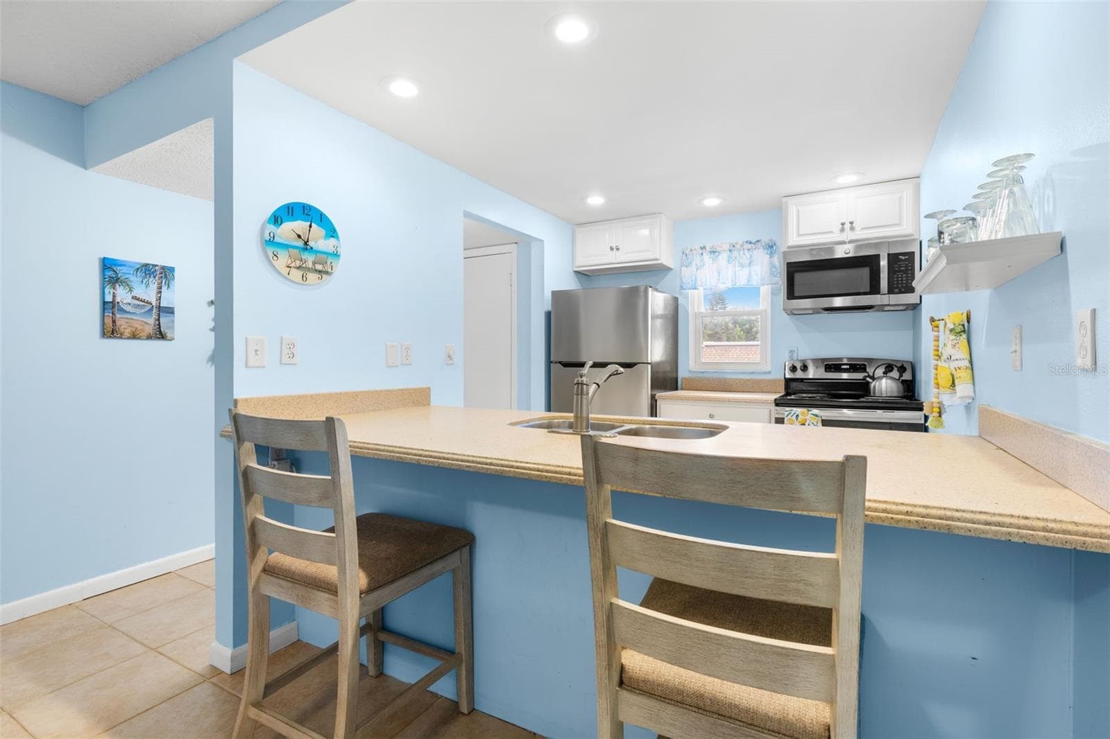 The kitchen wraps around a broad Corian breakfast bar with seating for two, with recessed lighting, a window over the rear counter and stainless-steel appliances including the refrigerator, range and microwave. - 12760 INDIAN ROCKS RD #107, LARGO