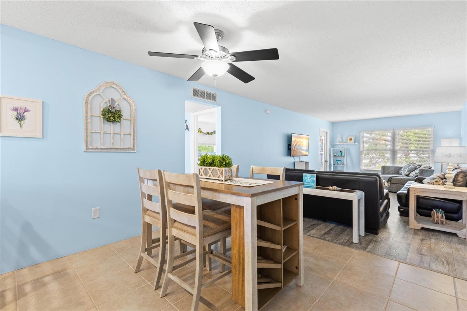 A second view of the dining area shows how naturally it opens into the living room, with tile flooring transitioning to luxury vinyl and a wide bank of windows bringing light into the far end of the space. - 12760 INDIAN ROCKS RD #107, LARGO