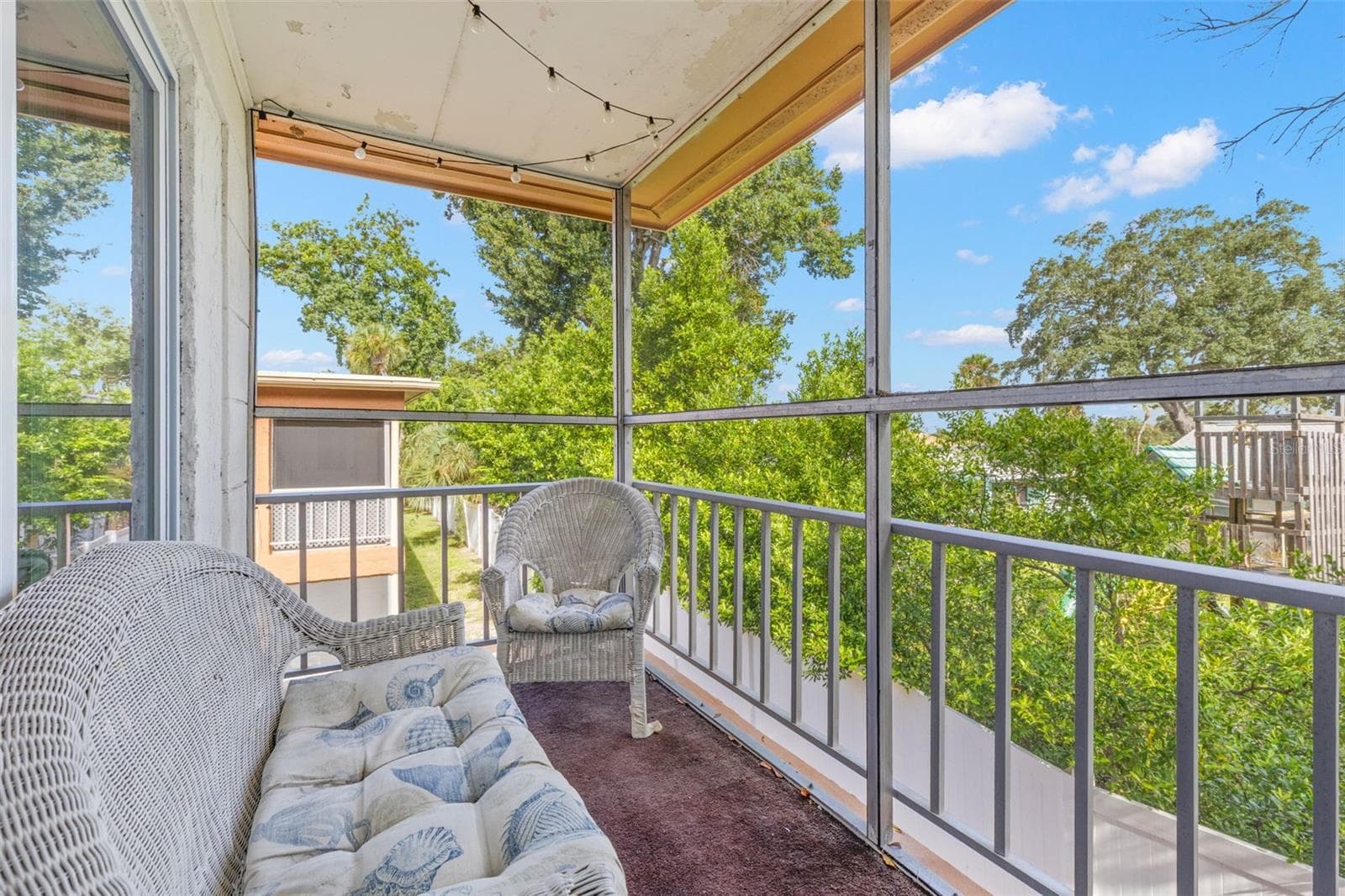 The screened balcony extends the living space outdoors, with room for seating and a leafy outlook framed by mature trees and open sky. - 12760 INDIAN ROCKS RD #107, LARGO