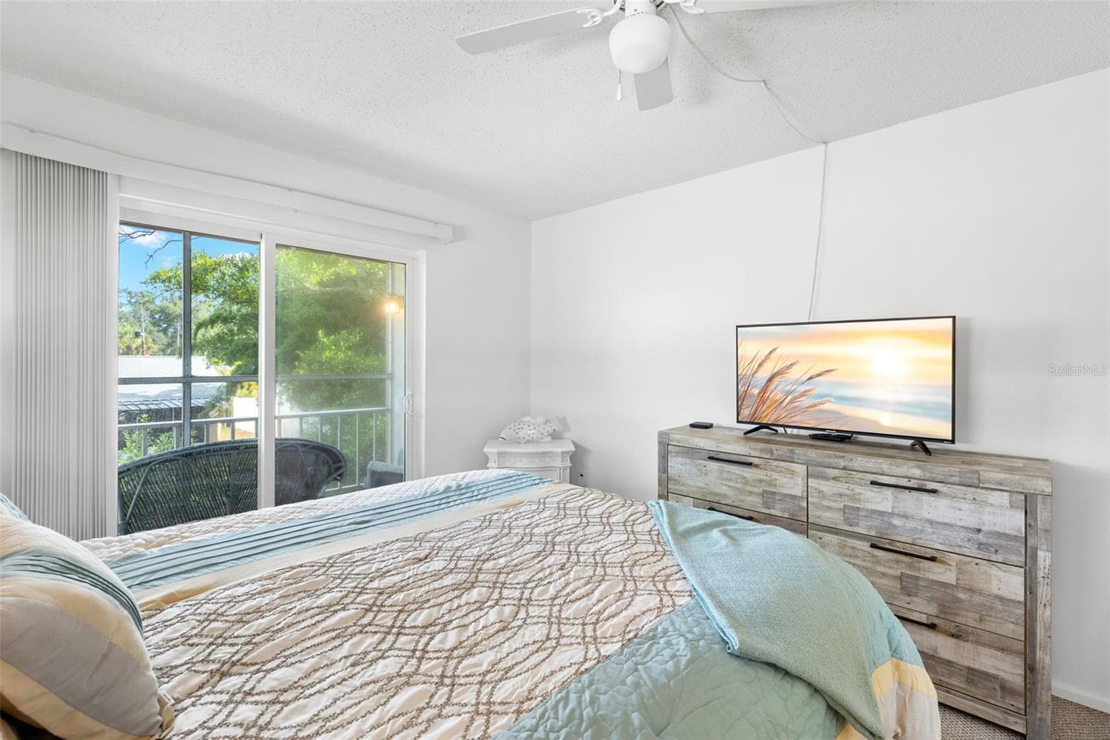 The primary bedroom measures approximately 14'9" x 11'3", with a ceiling fan overhead and sliding glass doors opening directly to the screened balcony and its leafy outlook. - 12760 INDIAN ROCKS RD #107, LARGO
