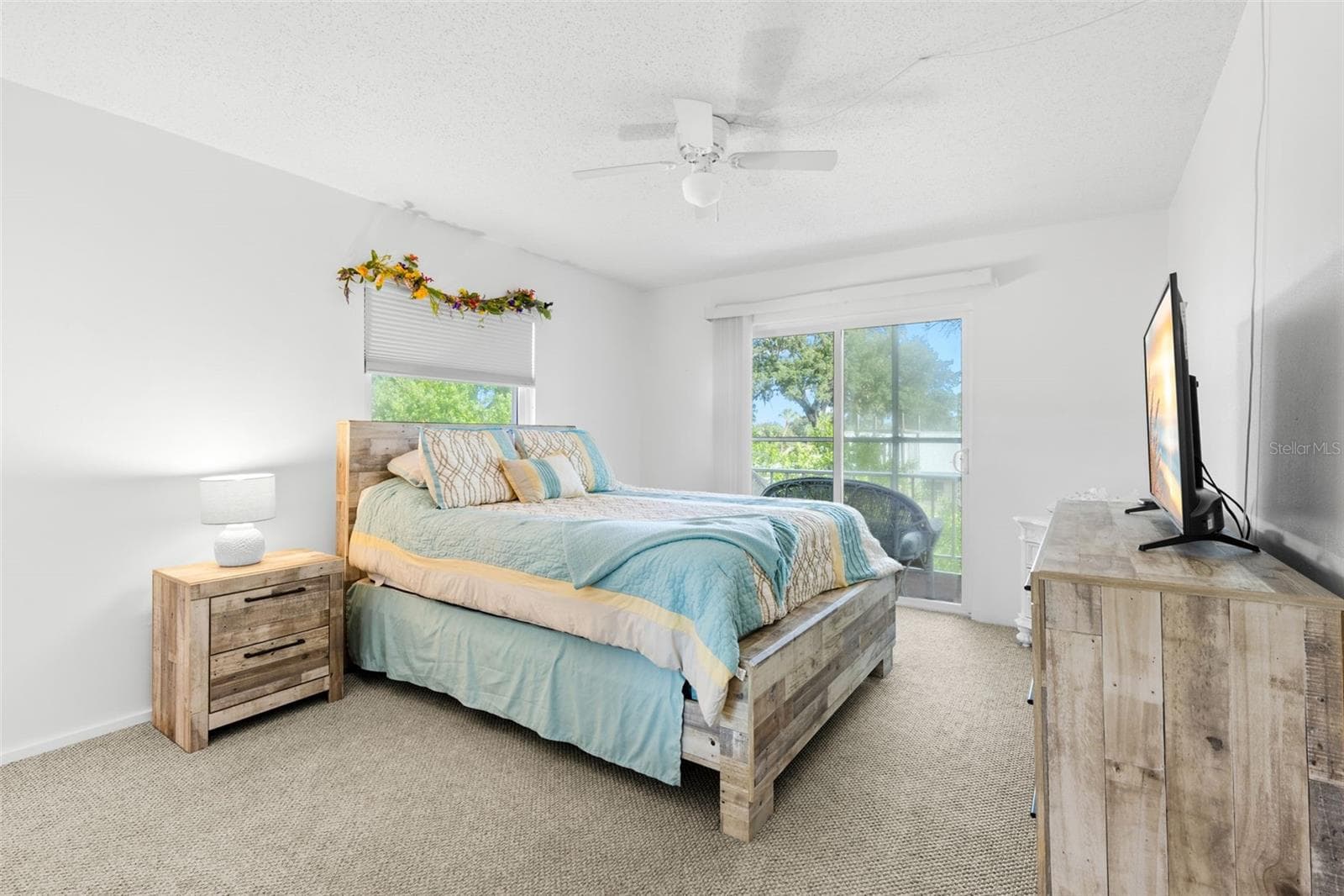 A neutral backdrop of light walls and carpet keeps the primary bedroom bright, while a second window and sliding glass doors bring in natural light and frame the greenery outside. - 12760 INDIAN ROCKS RD #107, LARGO