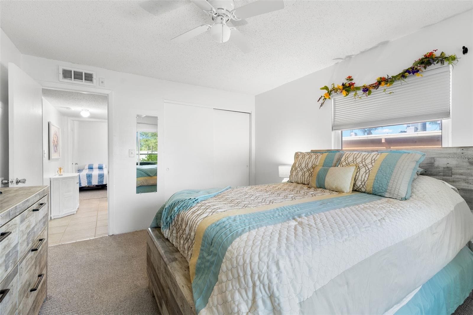 A built-in closet with sliding doors provides storage in the primary bedroom, while neutral carpet, a ceiling fan and a window complete the space. - 12760 INDIAN ROCKS RD #107, LARGO