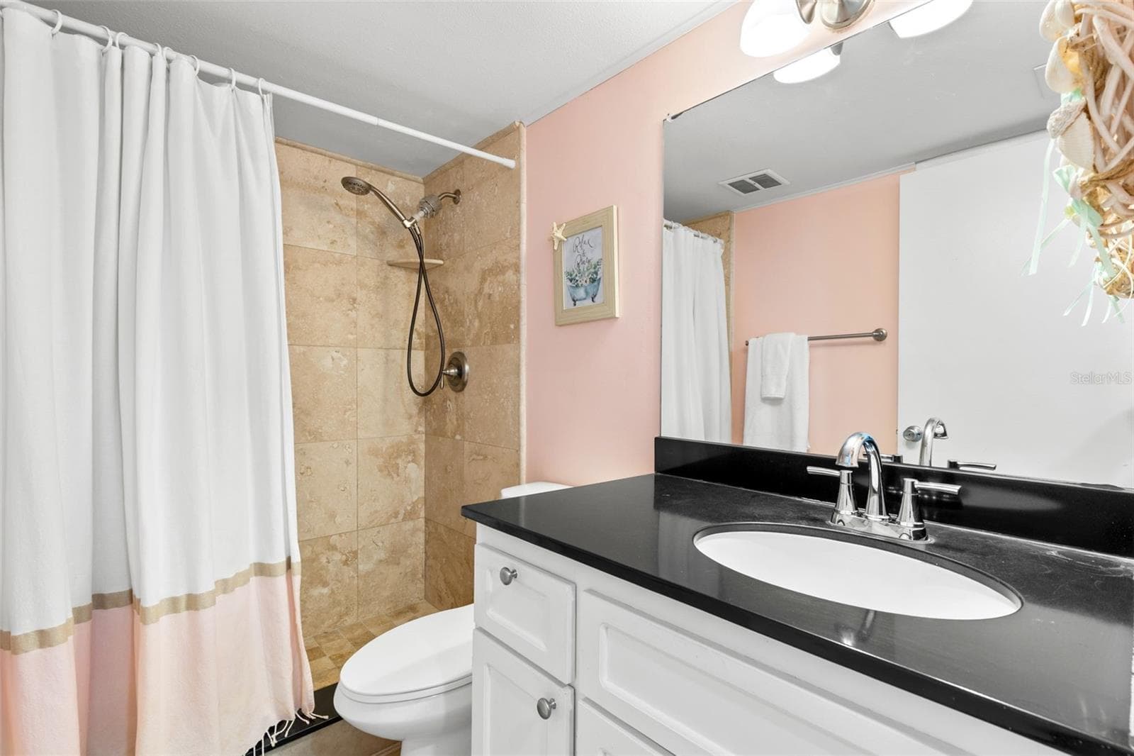 The bath pairs a dark countertop with light cabinetry and a large mirror, while the tub/shower is finished with tile surround and a handheld showerhead. - 12760 INDIAN ROCKS RD #107, LARGO