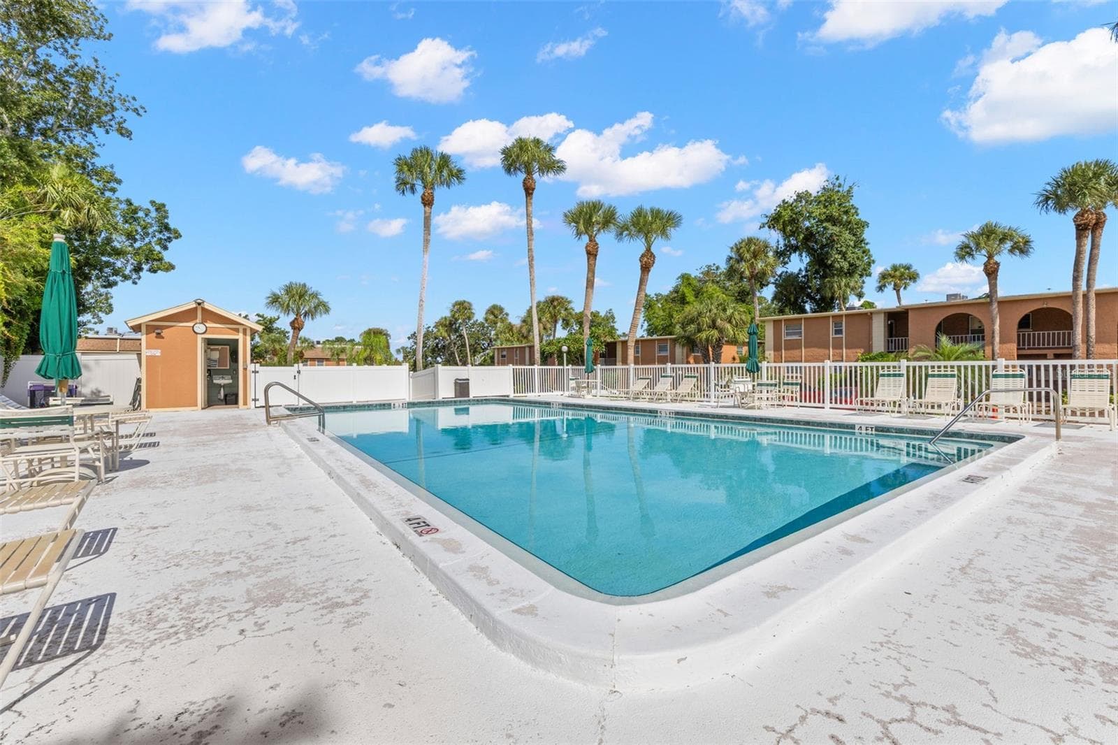 One of the community pools offers a spacious deck with plenty of lounge seating and umbrellas, framed by tall palms and the surrounding residential building. - 12760 INDIAN ROCKS RD #107, LARGO