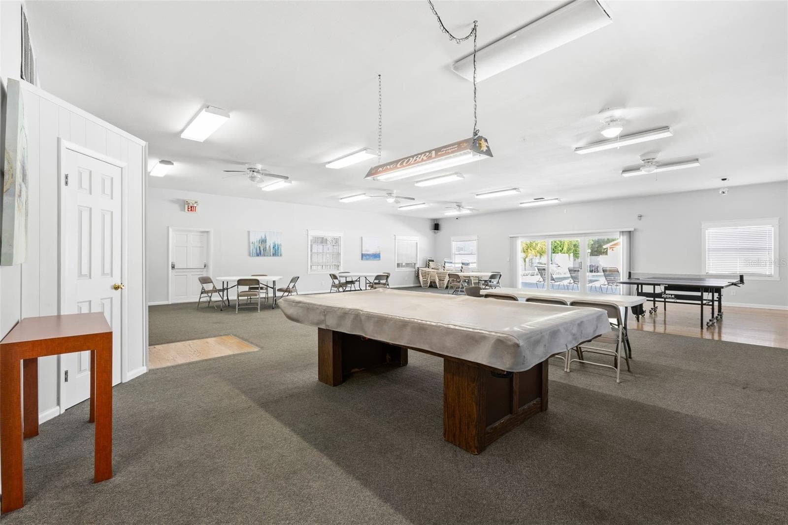 The clubhouse offers a large gathering space with billiards, ping-pong and multiple tables for games, cards or community events, with doors opening toward the pool area beyond. - 12760 INDIAN ROCKS RD #107, LARGO