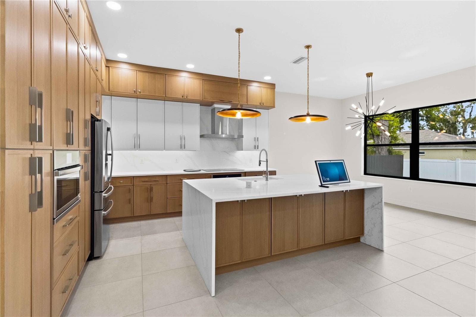 designer kitchen combines warmth and modern elegance with full-height wood cabinetry, quartz countertops, stainless-steel appliances, generous storage, and an oversized waterfall-edge island - 104 S MAKI RD, PLANT CITY